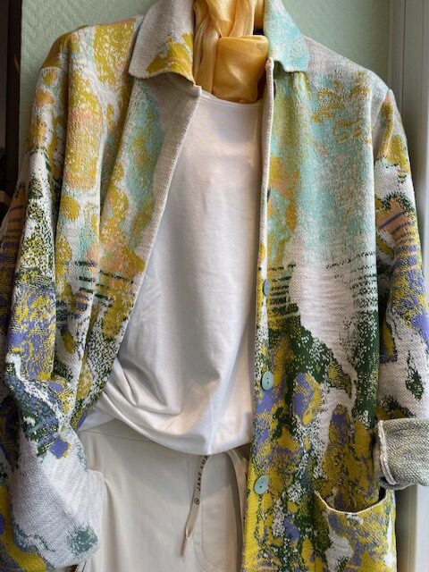 Bunte Strickjacke mit abstraktem Muster über weißem Hemd auf Schaufensterpuppe.