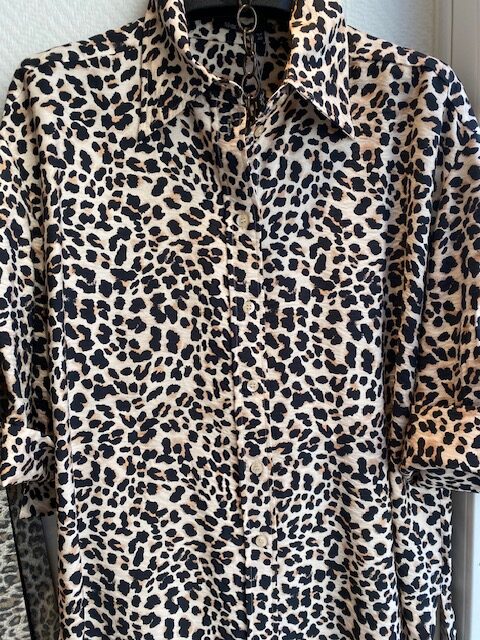 Ein Hemd mit Leopardenmuster in Schwarz und Beige, Kragen und Knopfleiste sichtbar.