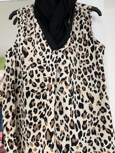 Ärmelloses Kleid mit Leopardenmuster, schwarzes Tuch darüber drapiert.