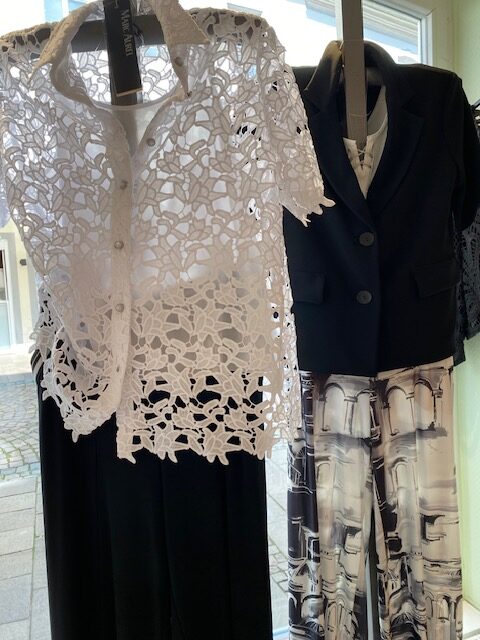 Eine weiße Spitzentunika und ein schwarzer Blazer mit abstrakten, gemusterten Hosen im Schaufenster.