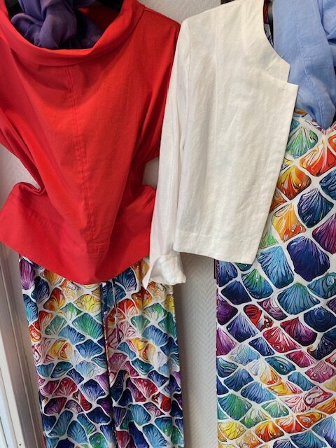 Bunte Kleidungsstücke: rote Bluse, weiße Jacke, beide mit farbig gemusterten Röcken.