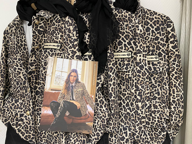 Eine Frau posiert selbstbewusst in Leopardenjacke vor einem Fenster.
