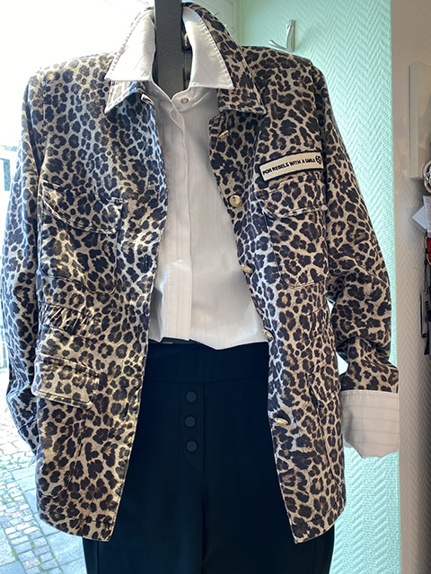 Ein Kleidungsstück auf einem Bügel zeigt ein Leopardenmuster-Sakko über einer weißen Bluse.