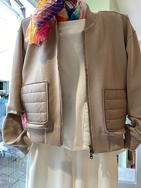 Ein Schaufensterpuppe trägt eine beige Bomberjacke mit buntem Schal.