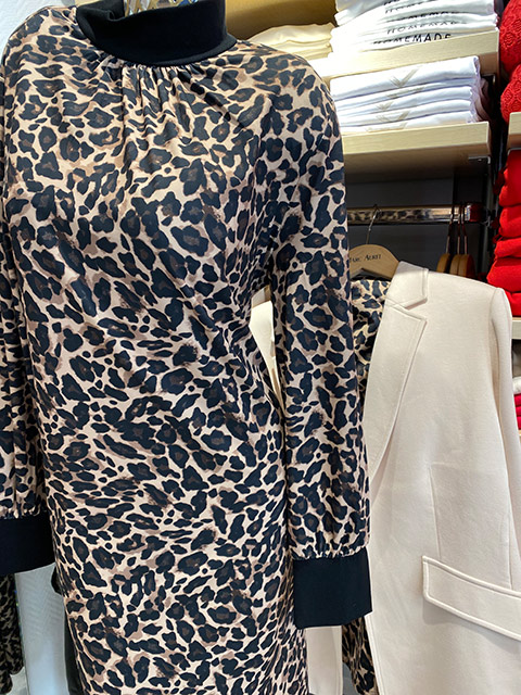 Ein elegantes Kleid mit auffälligem Leopardenmuster hängt neben einem beigen Mantel.