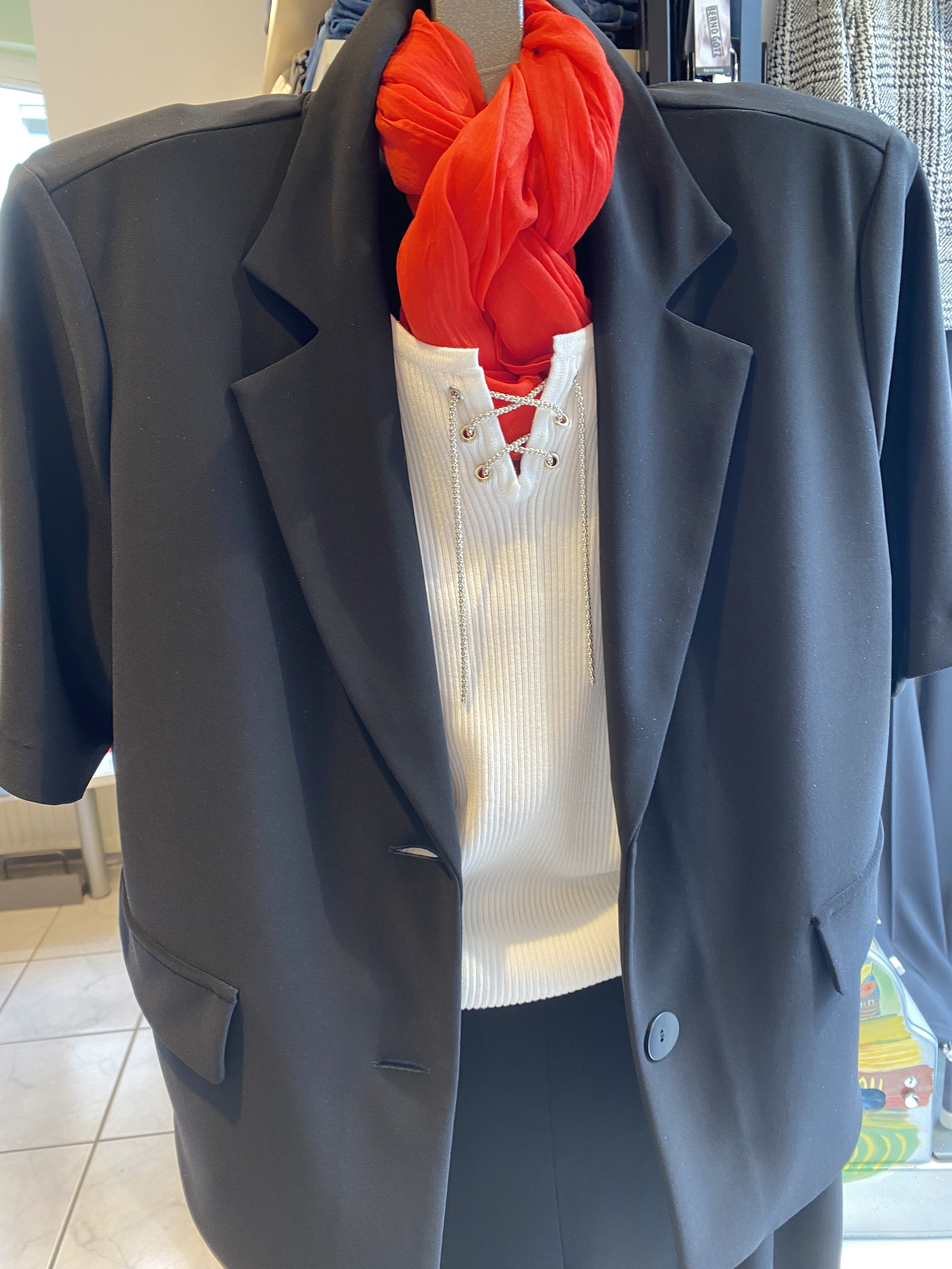 Ein schwarzes Jackett und ein rot-weißer Schal auf einem Kleiderbügel.
