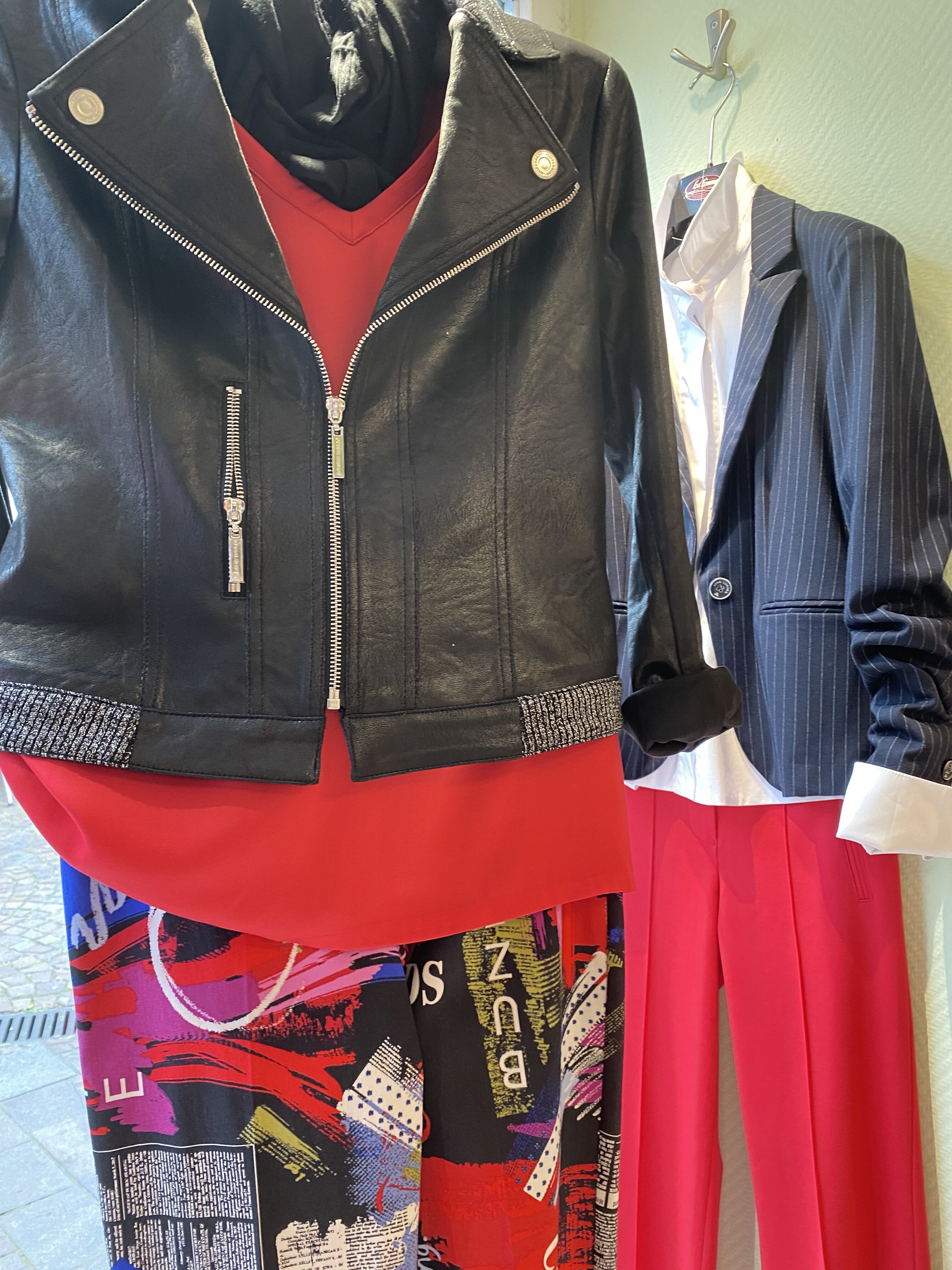 Ein Schaufenster mit einer schwarzen Jacke, einem roten Shirt und gemusterter Hose.