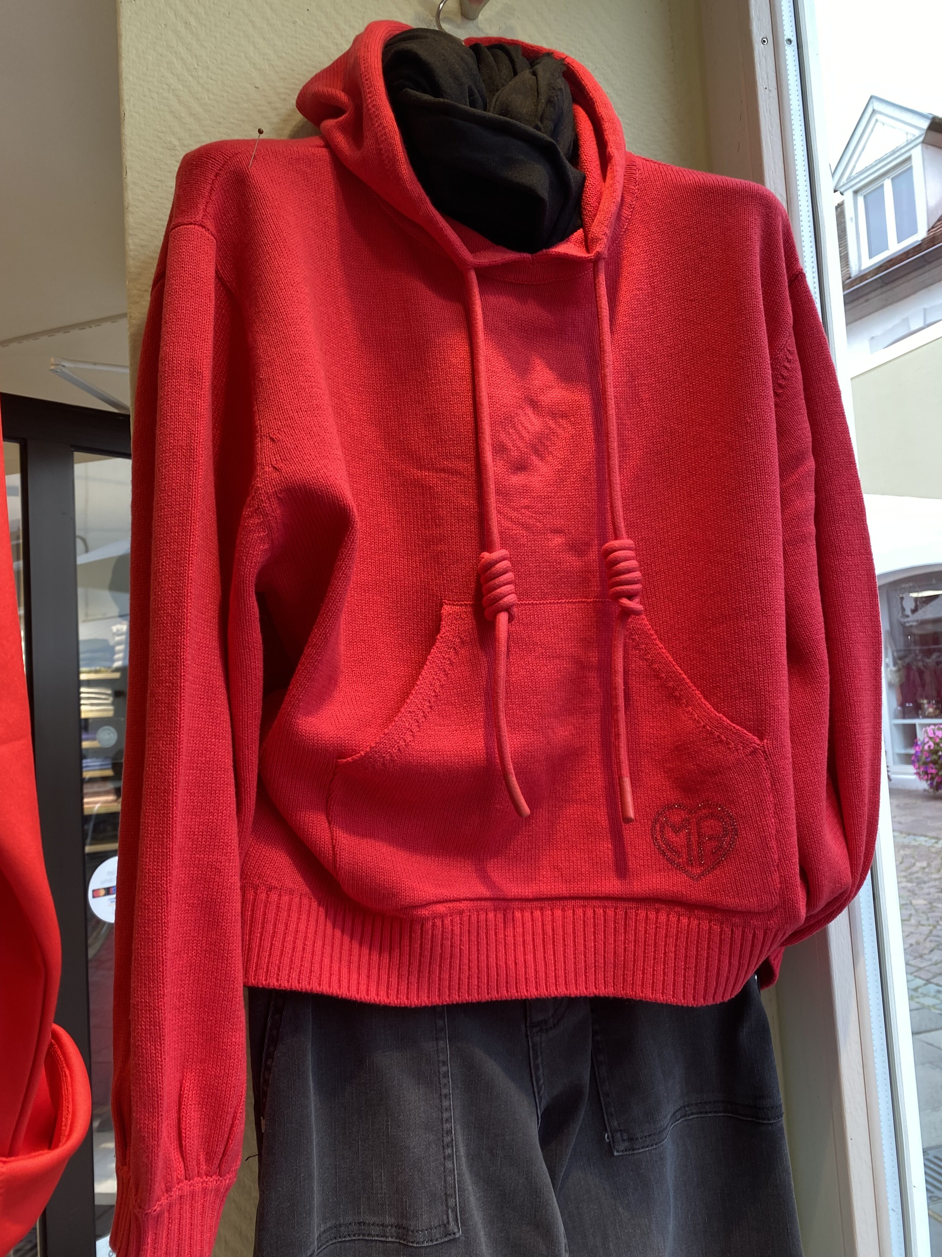 Roter Kapuzenpullover mit Herzstickerei, ausgestellt in einem Schaufenster.