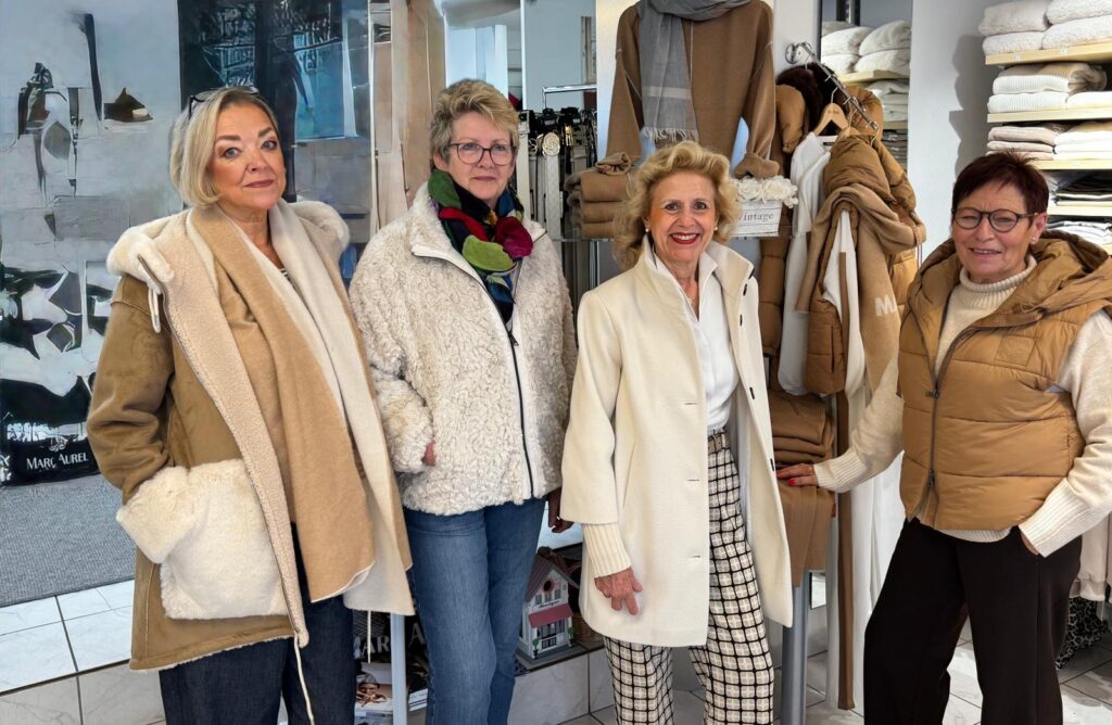 Vier ältere Damen in eleganten Wintermänteln lächeln kamerafreundlich.