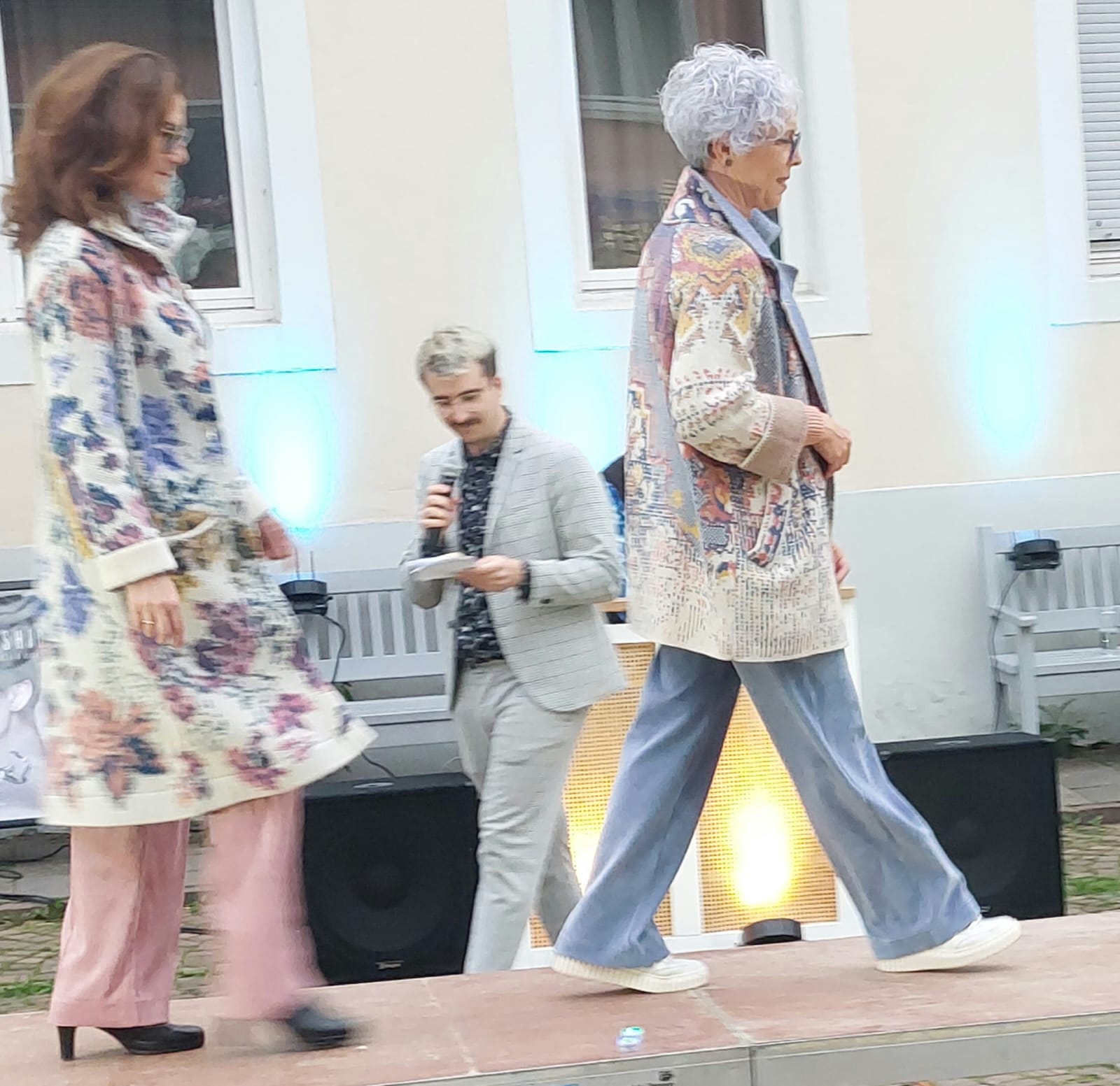 Zwei stilvoll gekleidete ältere Damen laufen mit ernster Miene auf einem Laufsteg