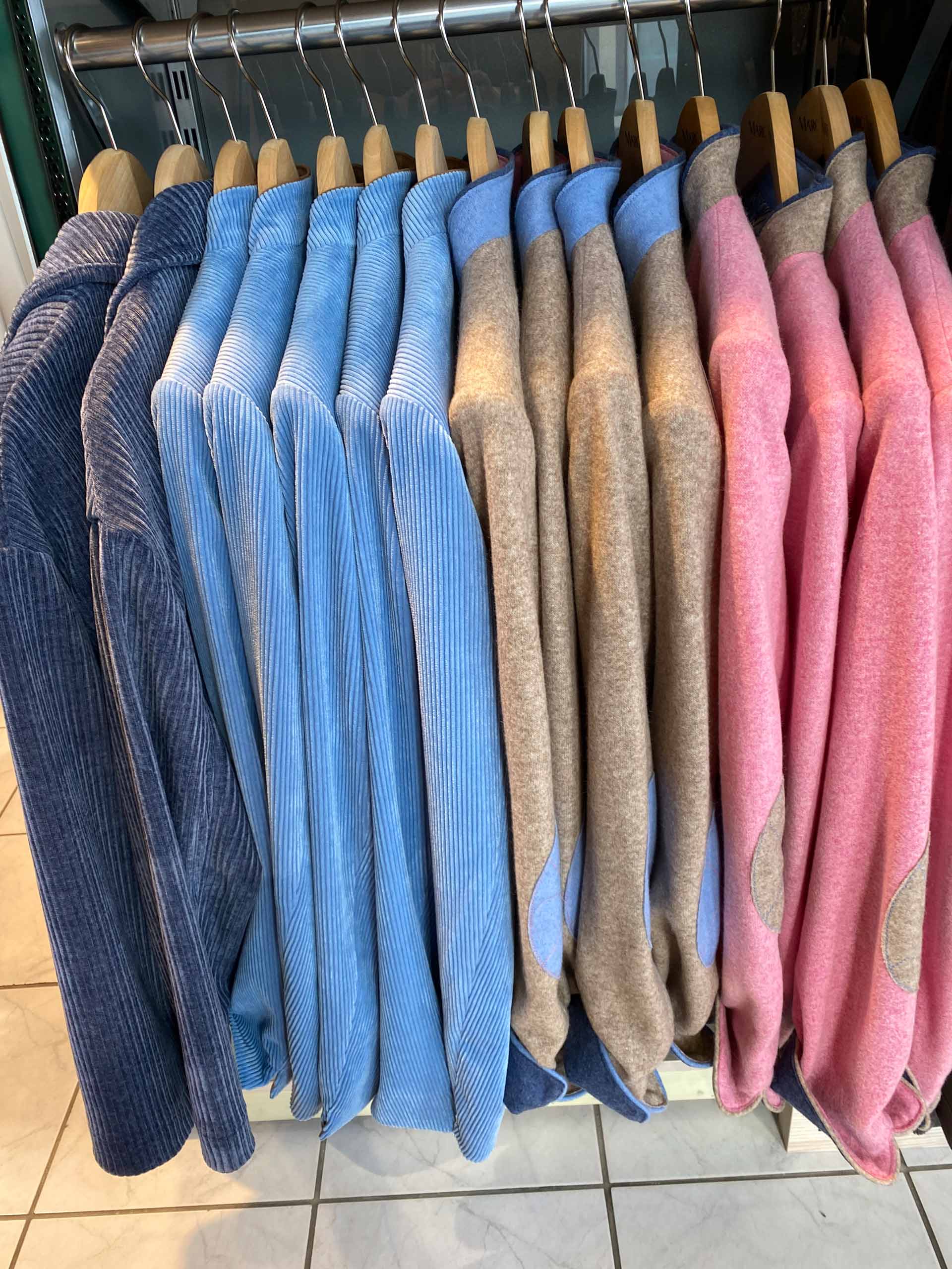 Mehrere Sakkos in Blau, Beige und Rosa hängen ordentlich auf Holzkleiderbügeln