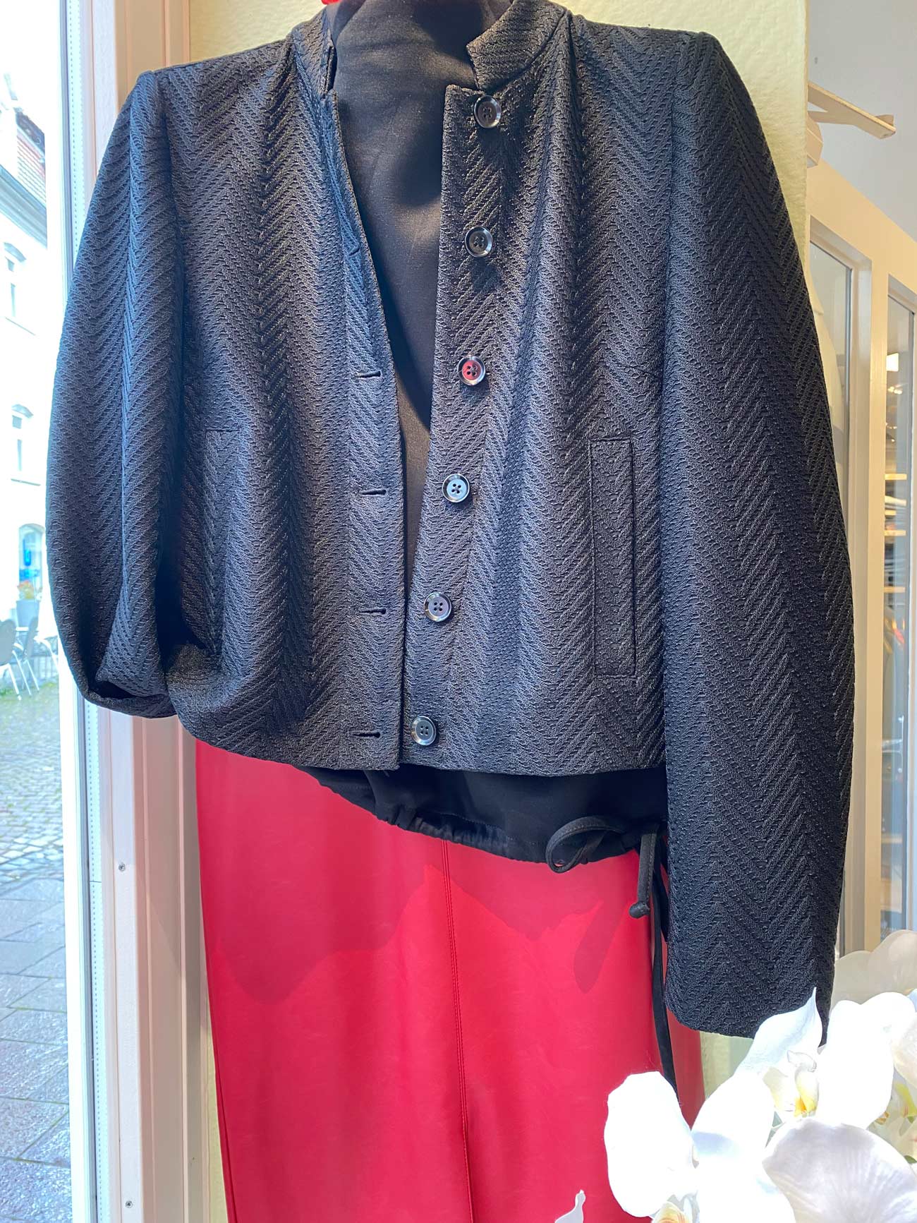 Eine schwarze strukturierte Jacke auf einer Schaufensterpuppe mit roten Hosen