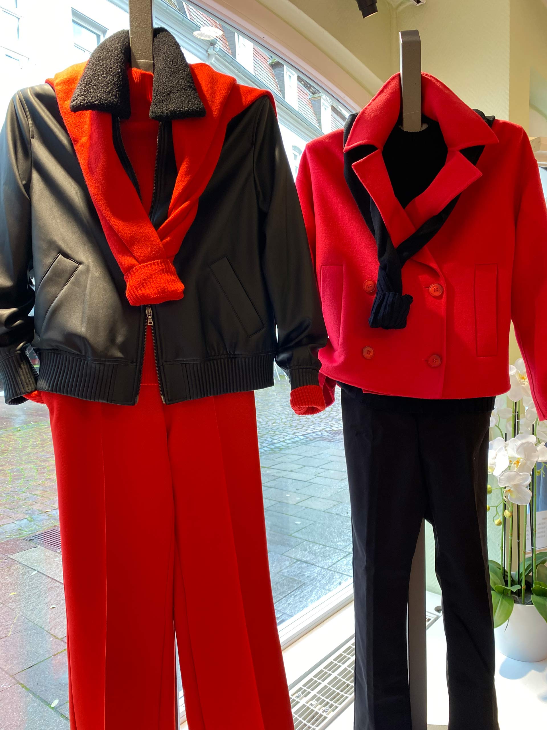 Zwei Schaufensterpuppen mit roten und schwarzen eleganten Outfits vor einem Fenster