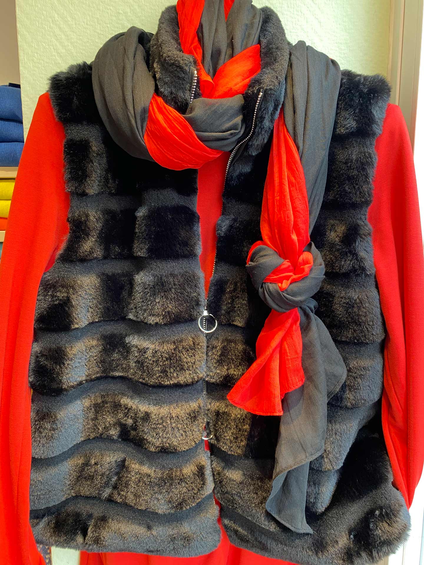 Rote Bluse mit schwarzer Fellweste und grau-rotem Schal elegant drapiert
