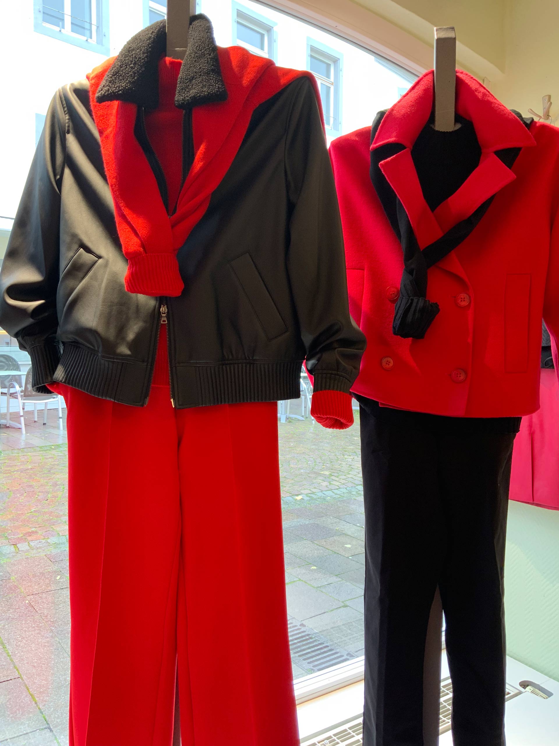 Zwei Schaufensterpuppen tragen auffällige rot-schwarze Outfits mit Jacken und Hosen