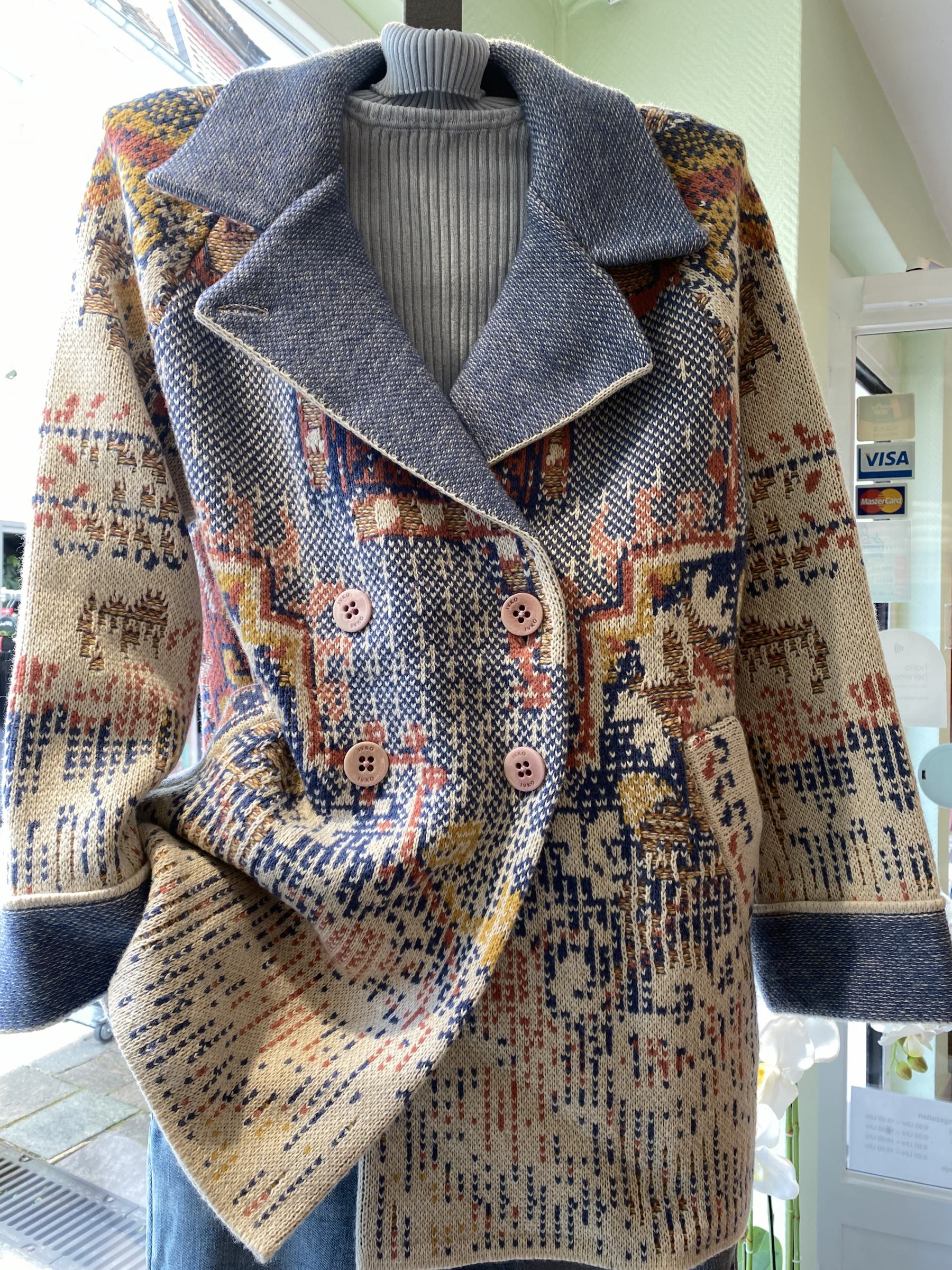 Eine Schaufensterpuppe trägt einen gemusterten Mantel mit bunten Details und Kragen