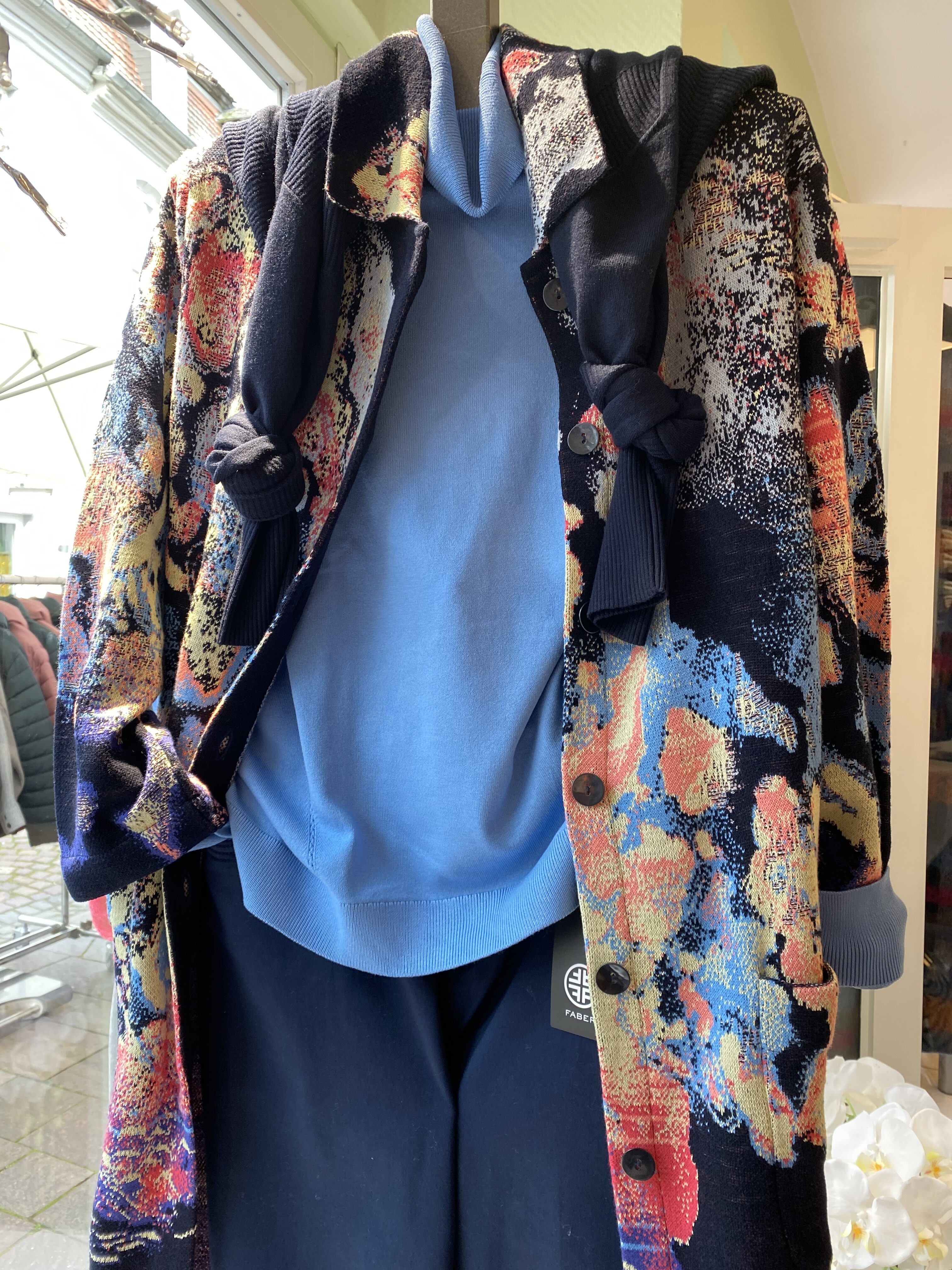 Eine Schaufensterpuppe trägt einen bunten Mantel über einem hellblauen Pullover und dunkelblauer Hose
