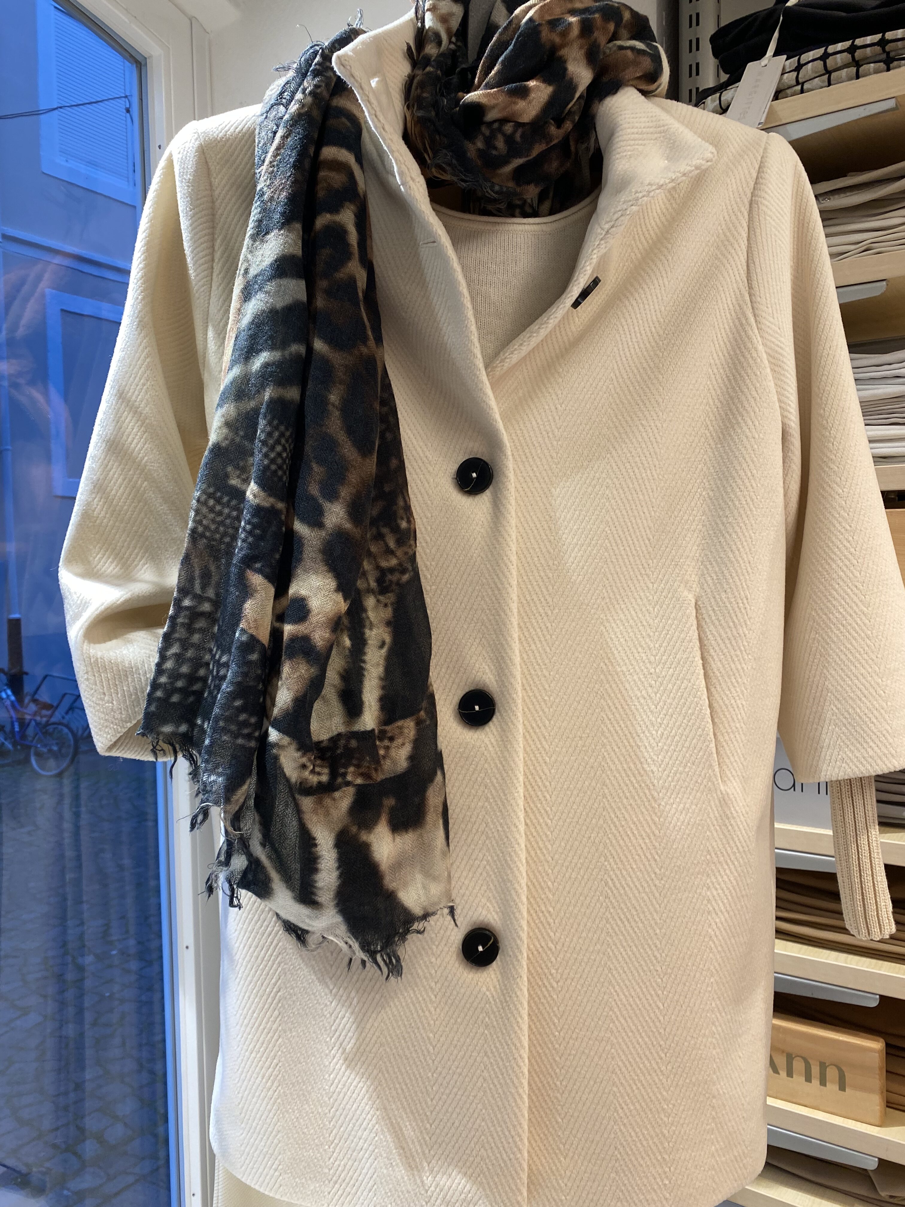Eine cremefarbene Jacke mit großen schwarzen Knöpfen und gemustertem Schal