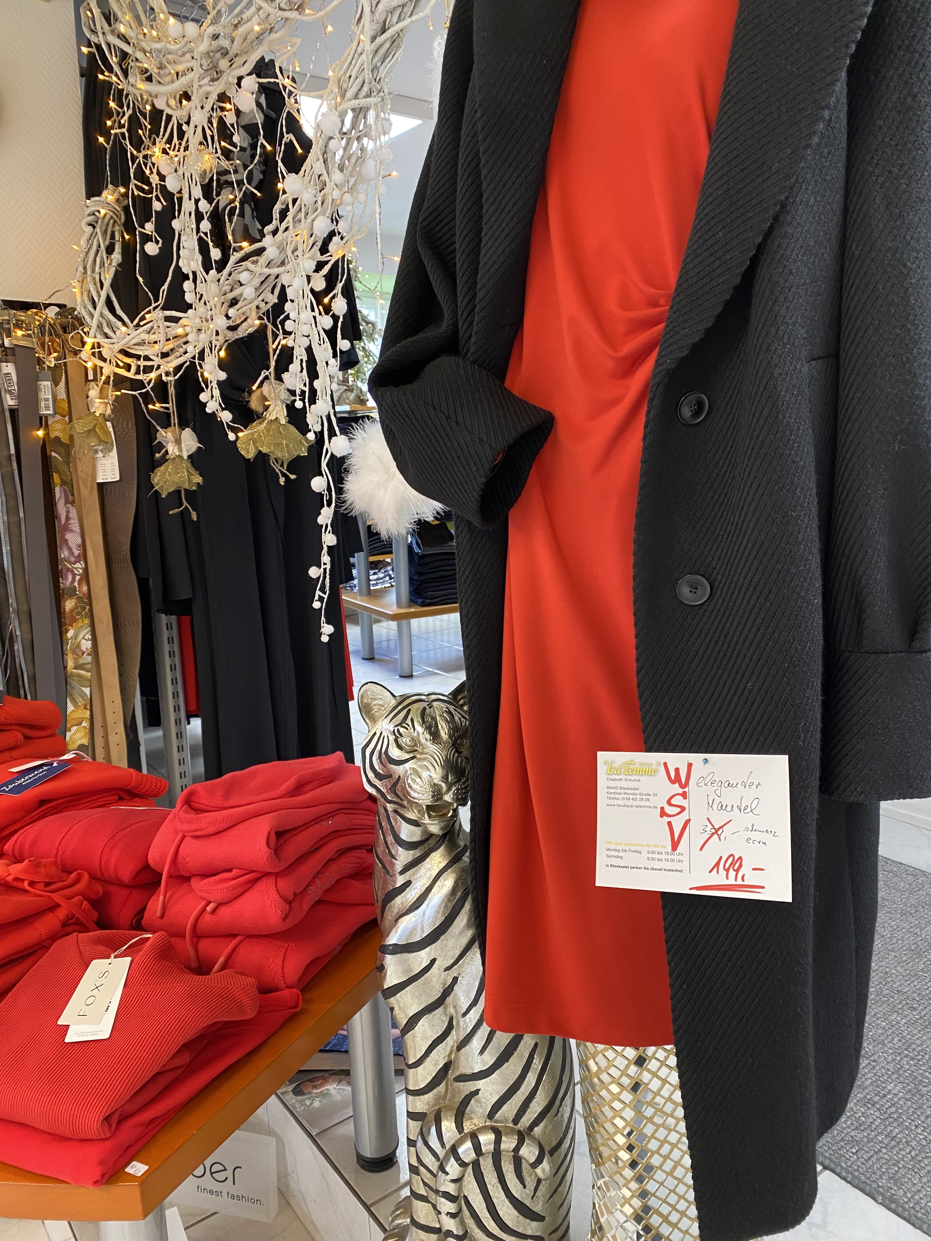 Eine Schaufensterpuppe trägt ein elegantes rotes Kleid mit schwarzem Mantel neben einem Tigerdekor