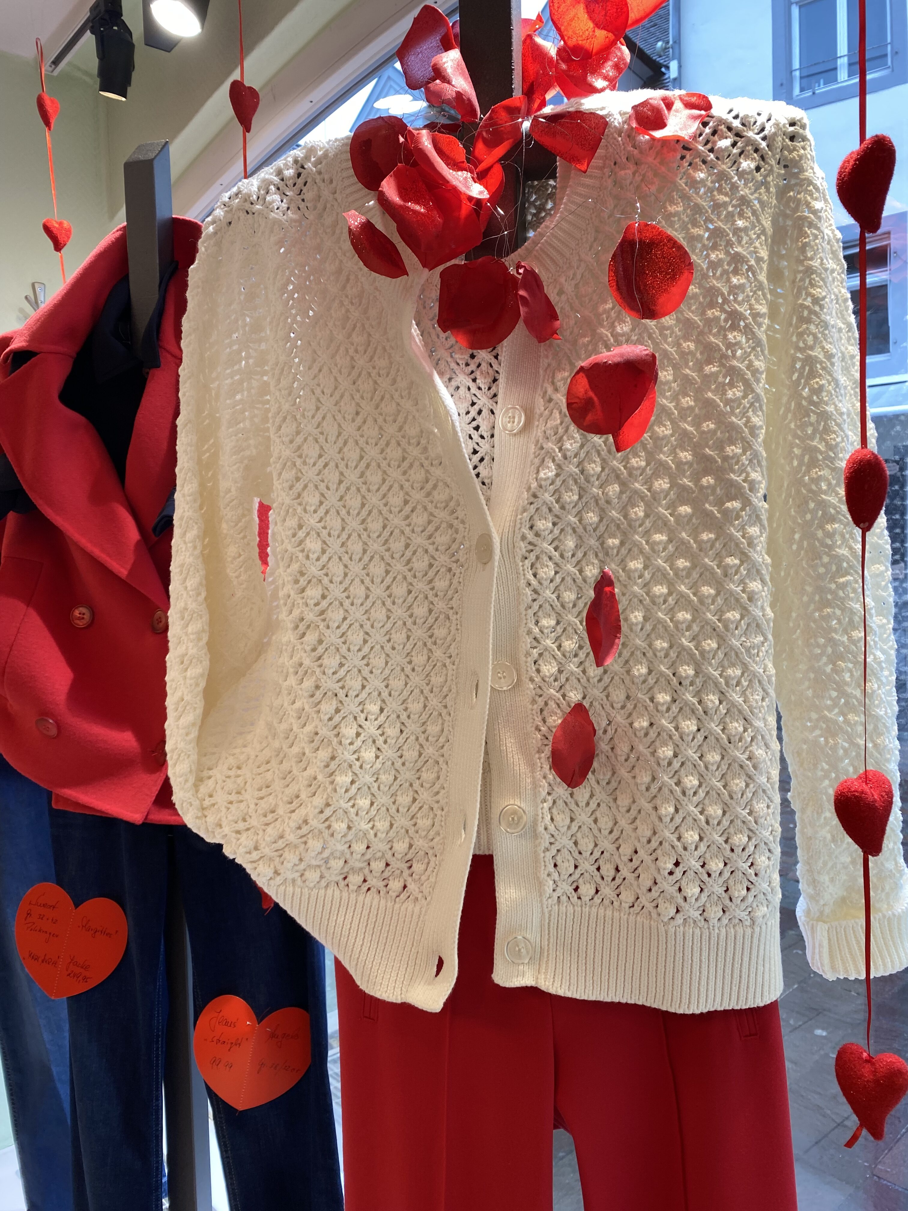 Eine cremefarbene, grob gestrickte Strickjacke hängt mit roten Herzen dekoriert