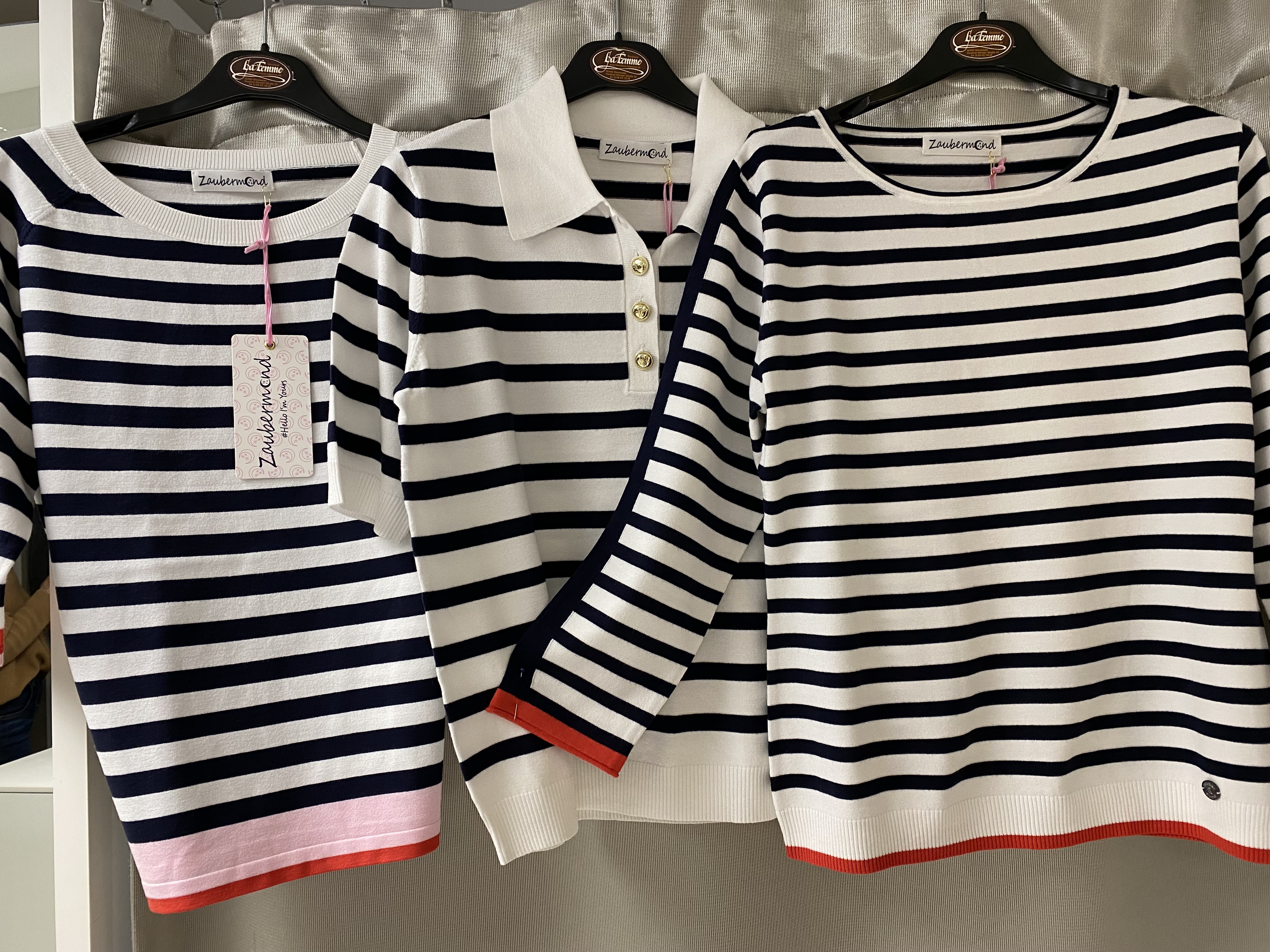 Drei gestreifte Pullover in Schwarz Weiß mit roten Details hängen nebeneinander