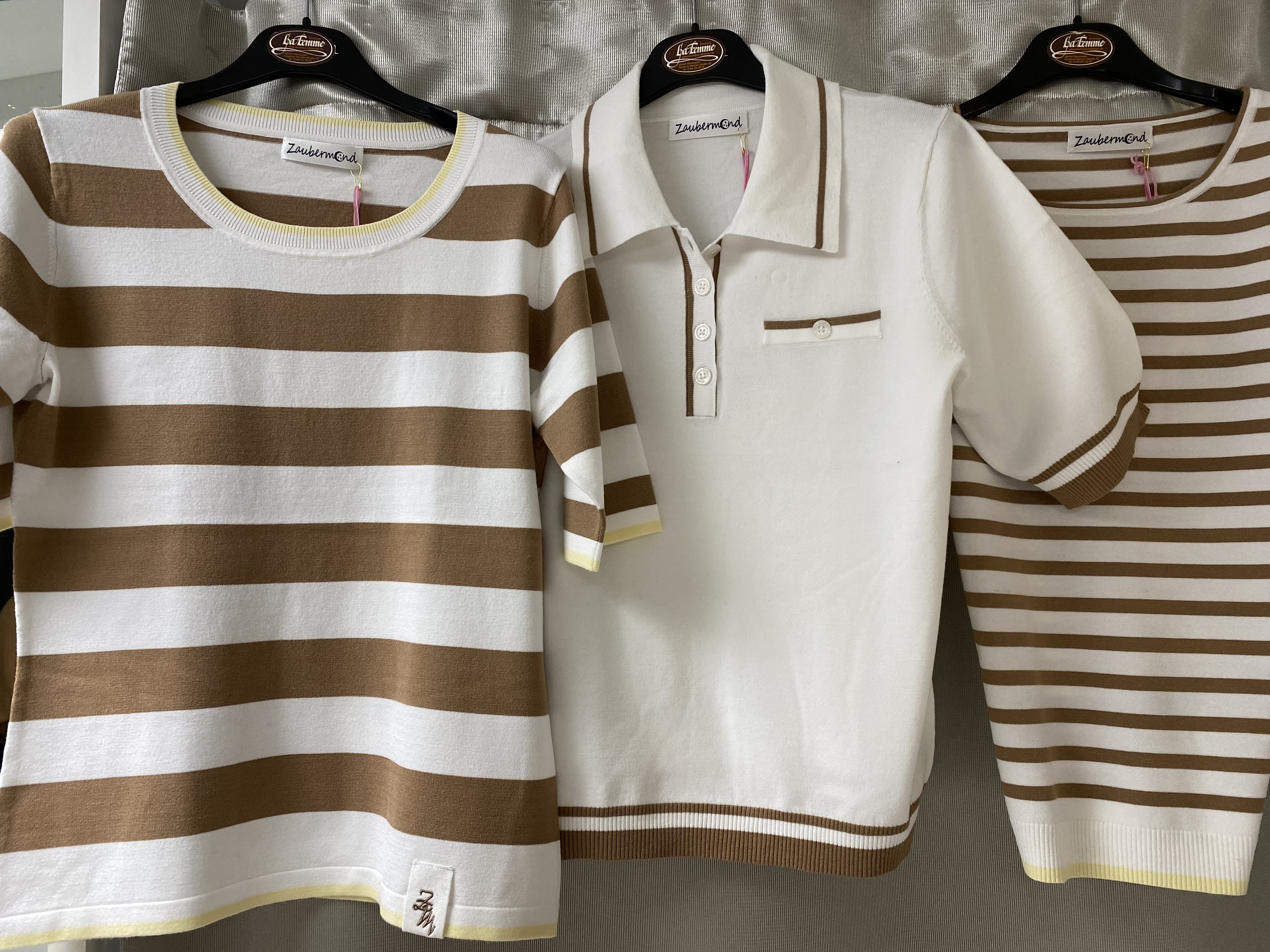 Drei beige und weiße Oberteile mit Streifen und unterschiedlichen Kragen an Bügeln