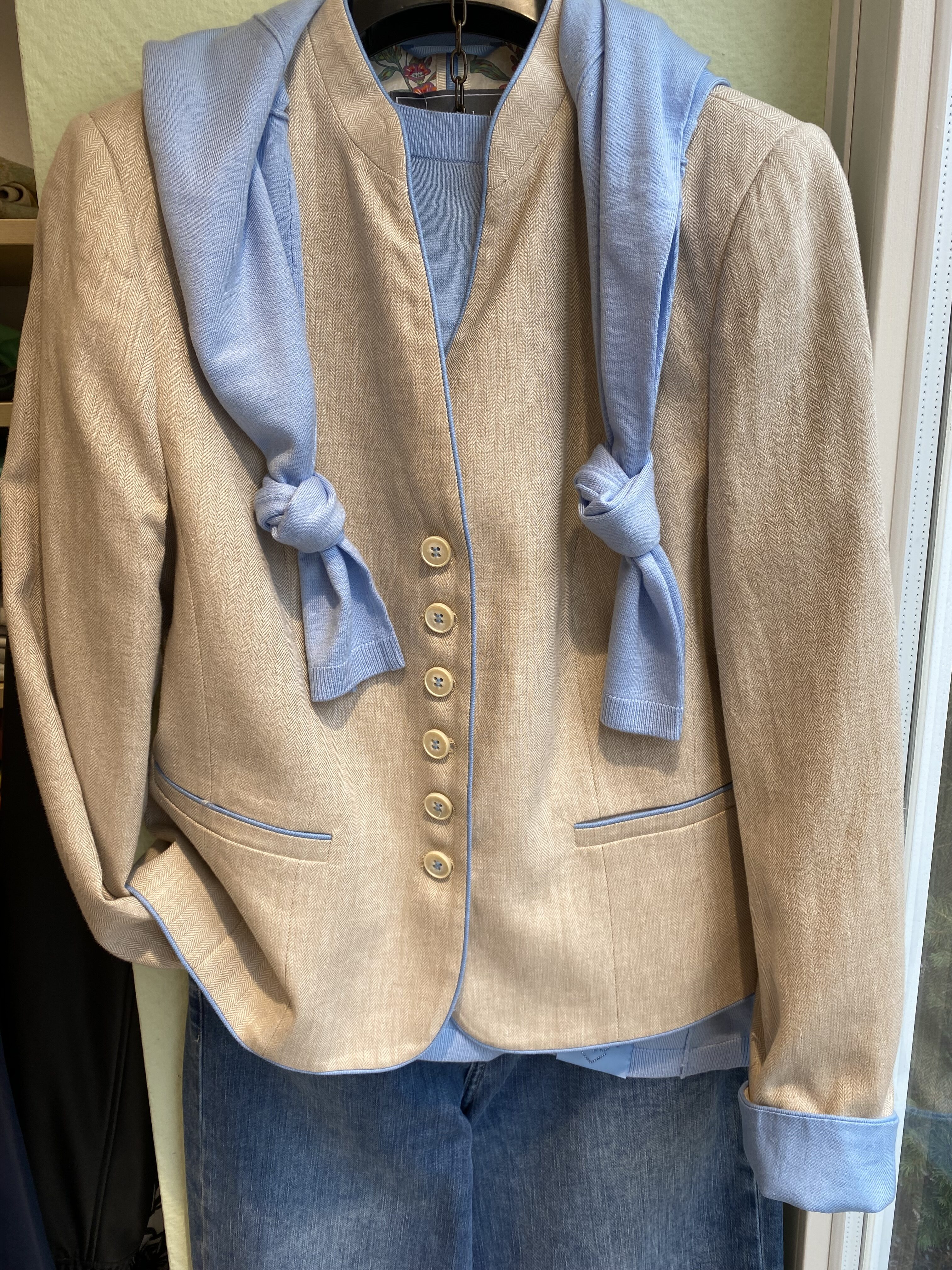 Beiger Blazer mit goldenen Knöpfen und hellblauem Pullover lässig darüber drapiert