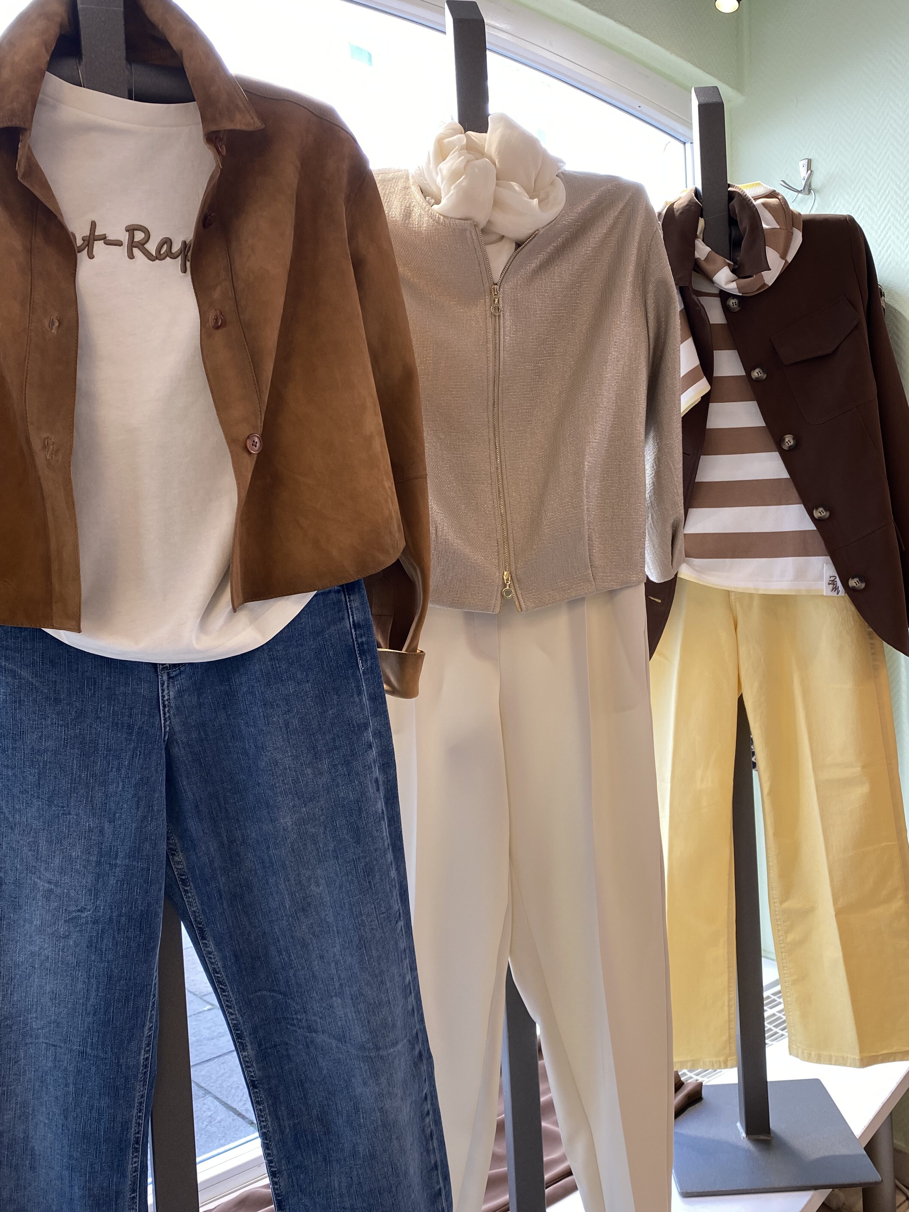 Drei Schaufensterpuppen zeigen modische Outfits in Braun, Beige und Gelb mit lockerer Haltung