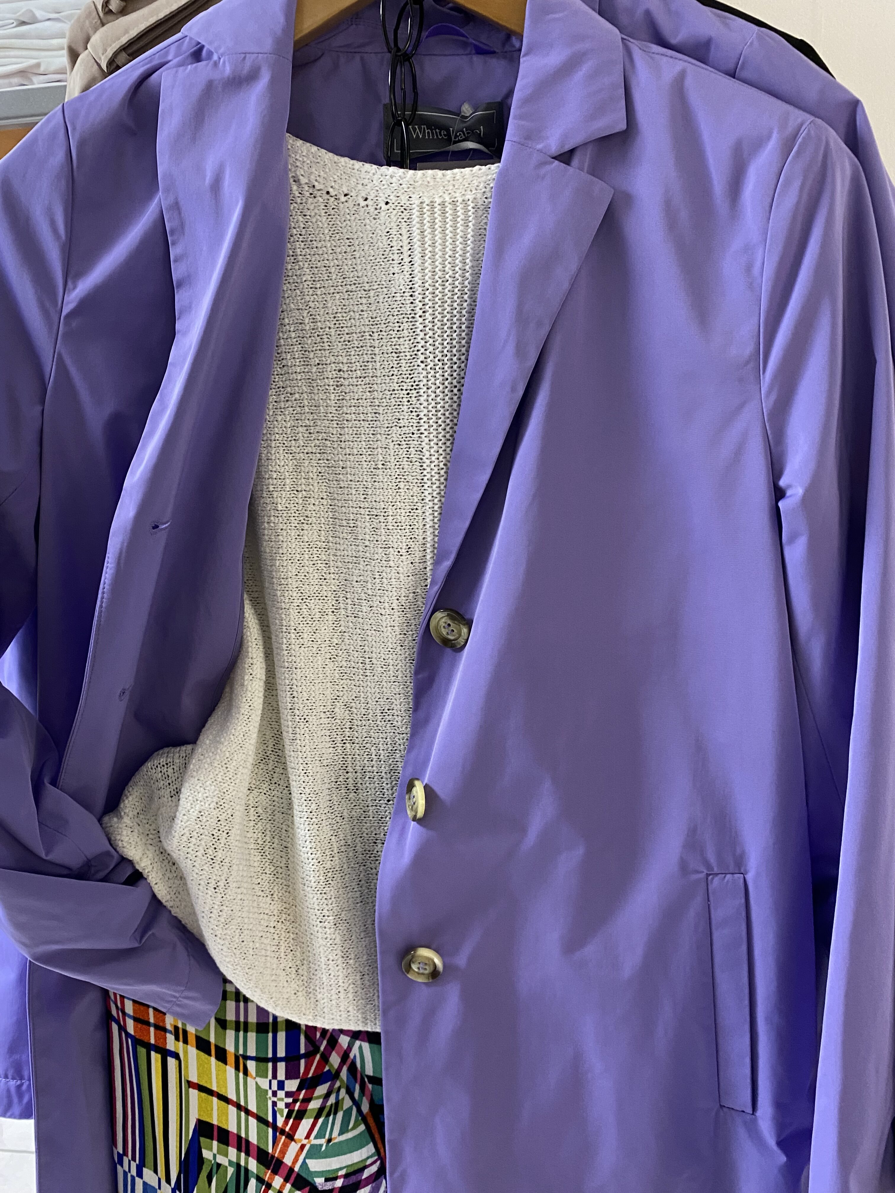 Lila Sakko mit drei Knöpfen über weißem Strickpulli und bunter Karohose