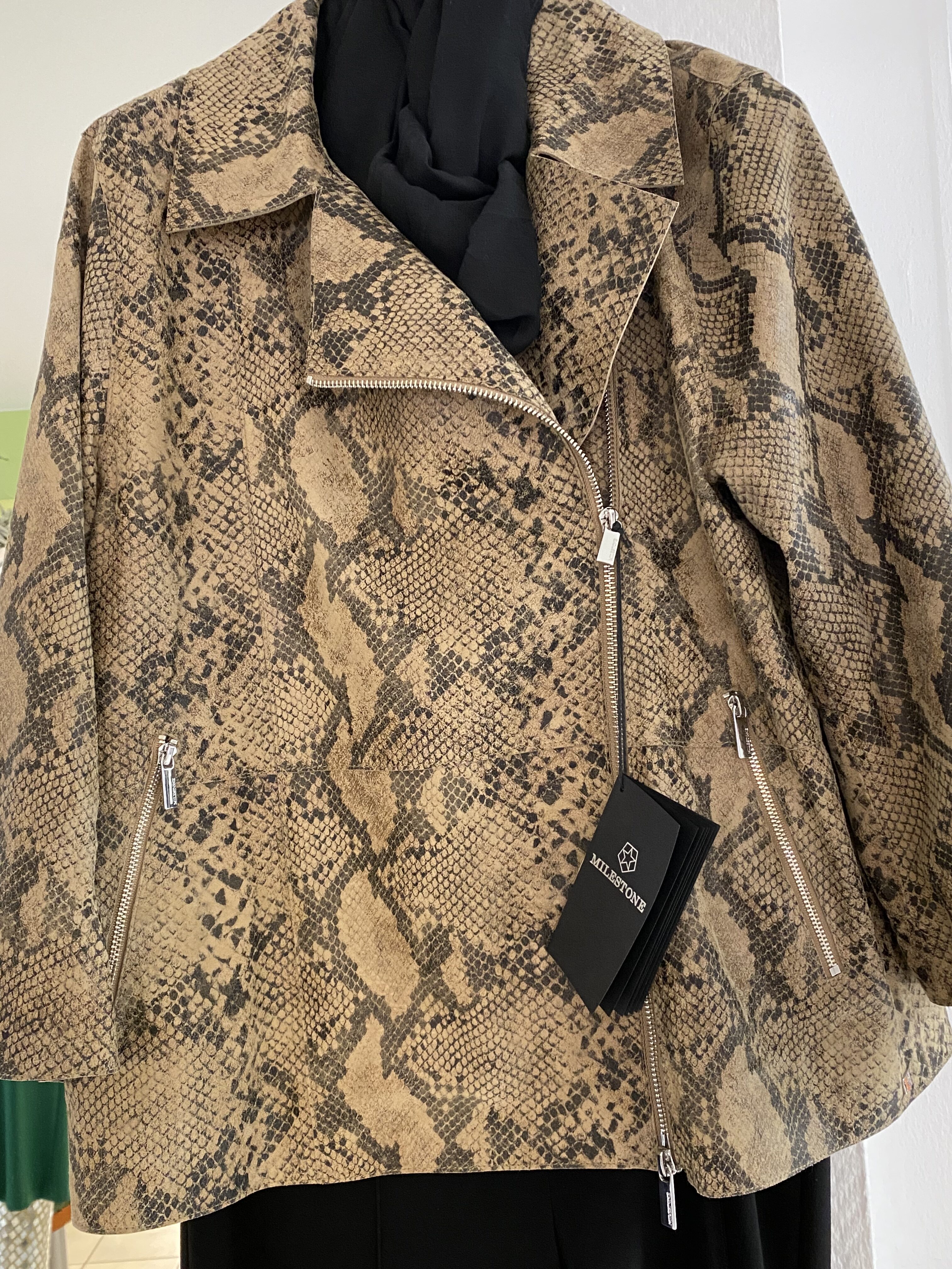Eine beige Jacke mit Schlangenledermuster und auffälligen silbernen Reißverschlüssen