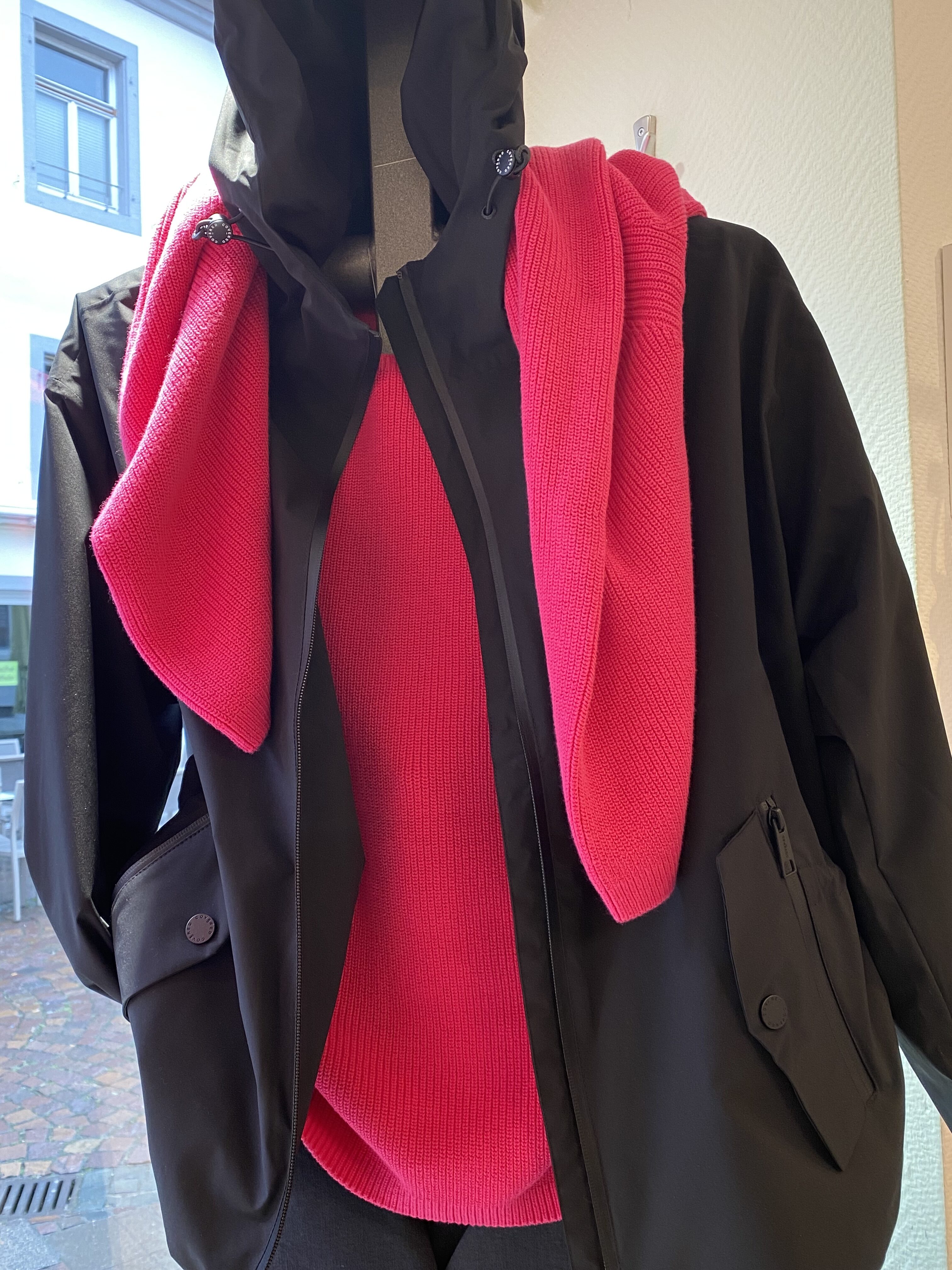 Eine Schaufensterpuppe trägt eine schwarze Jacke und einen leuchtend pinken Pullover