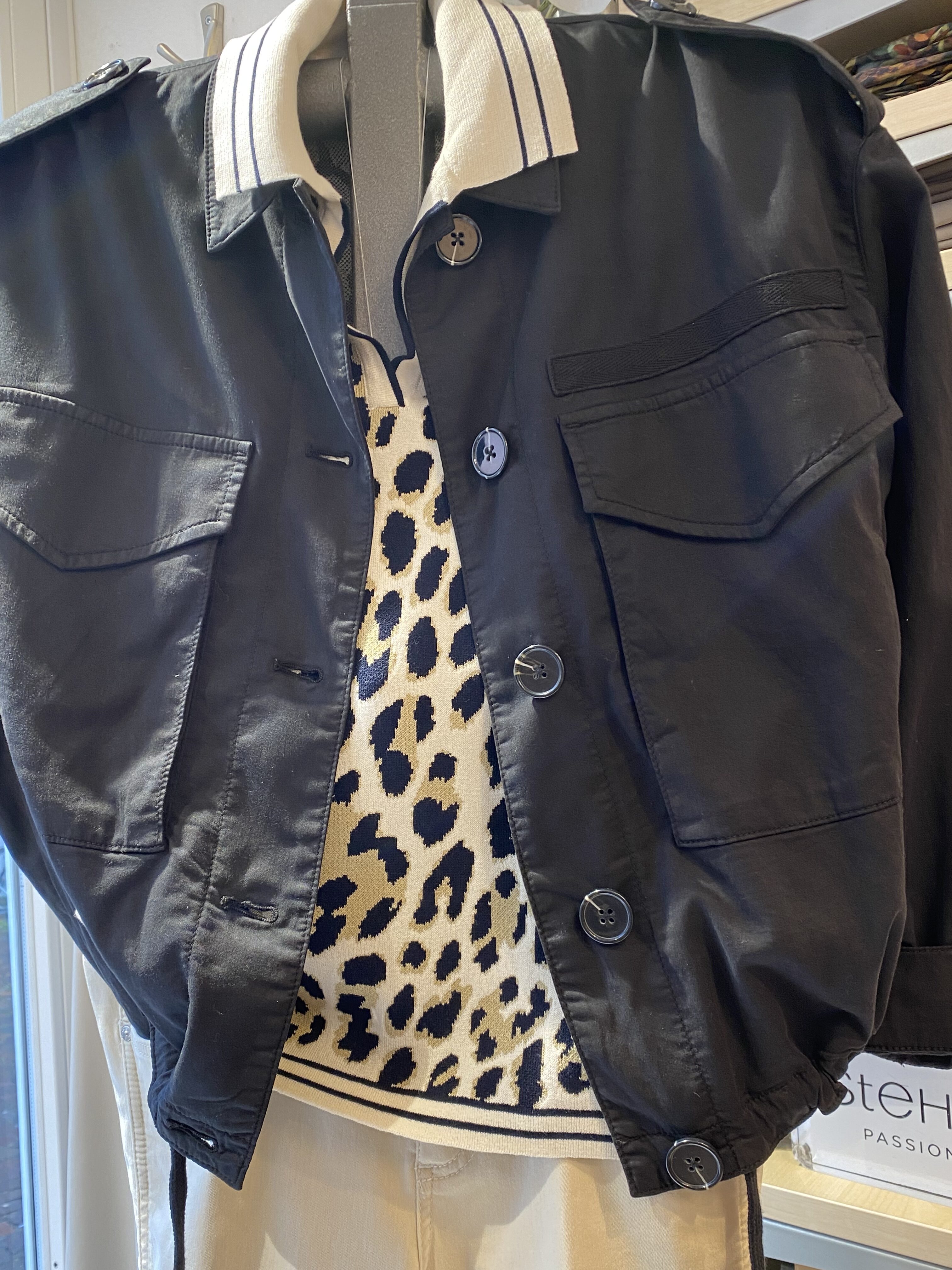 Person trägt schwarze Jacke über einem cremefarbenen Pulli mit Leopardenmuster