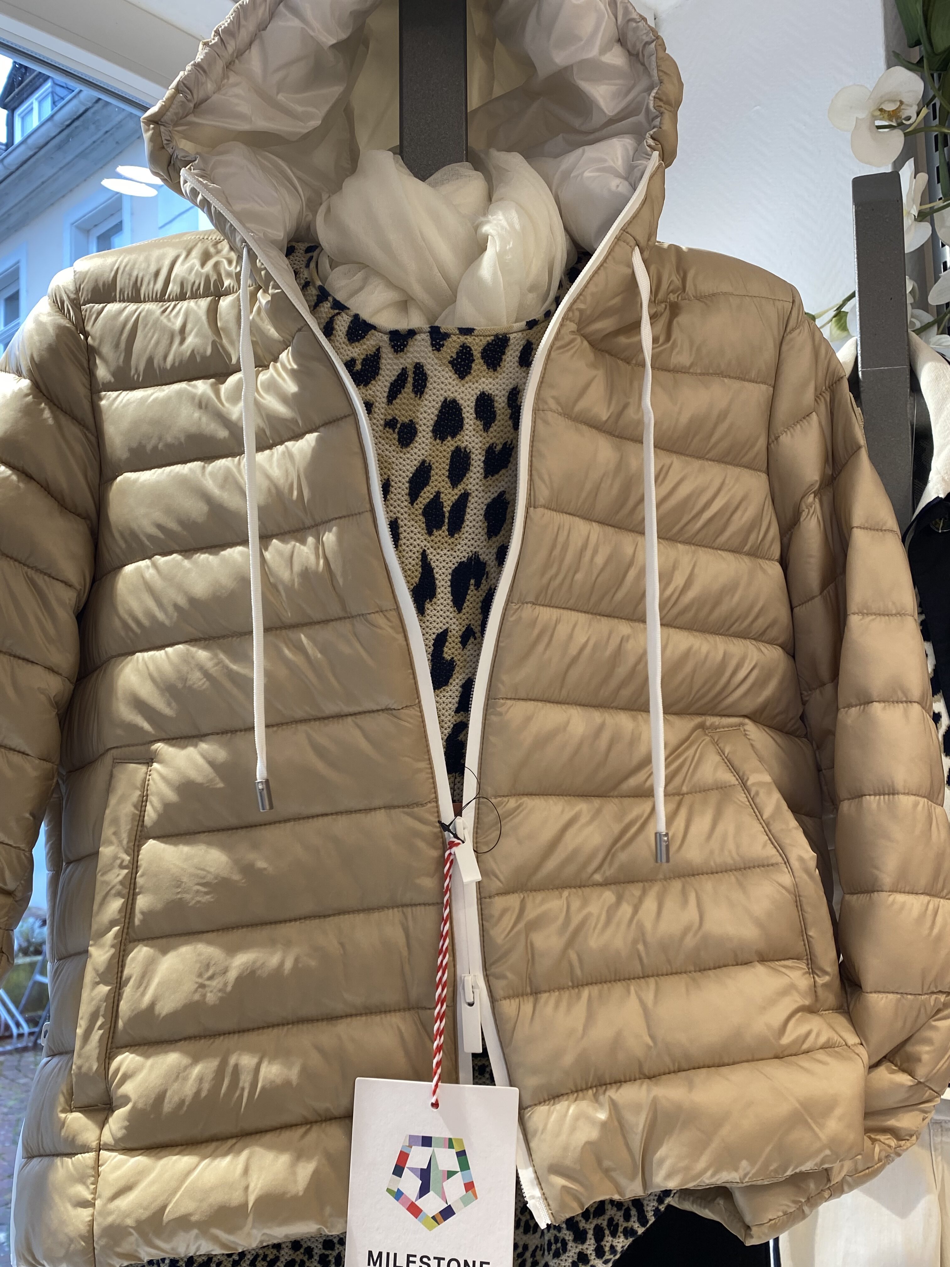 Beigefarbene Steppjacke mit weißem Reißverschluss über einem Leopardenmusterpullover
