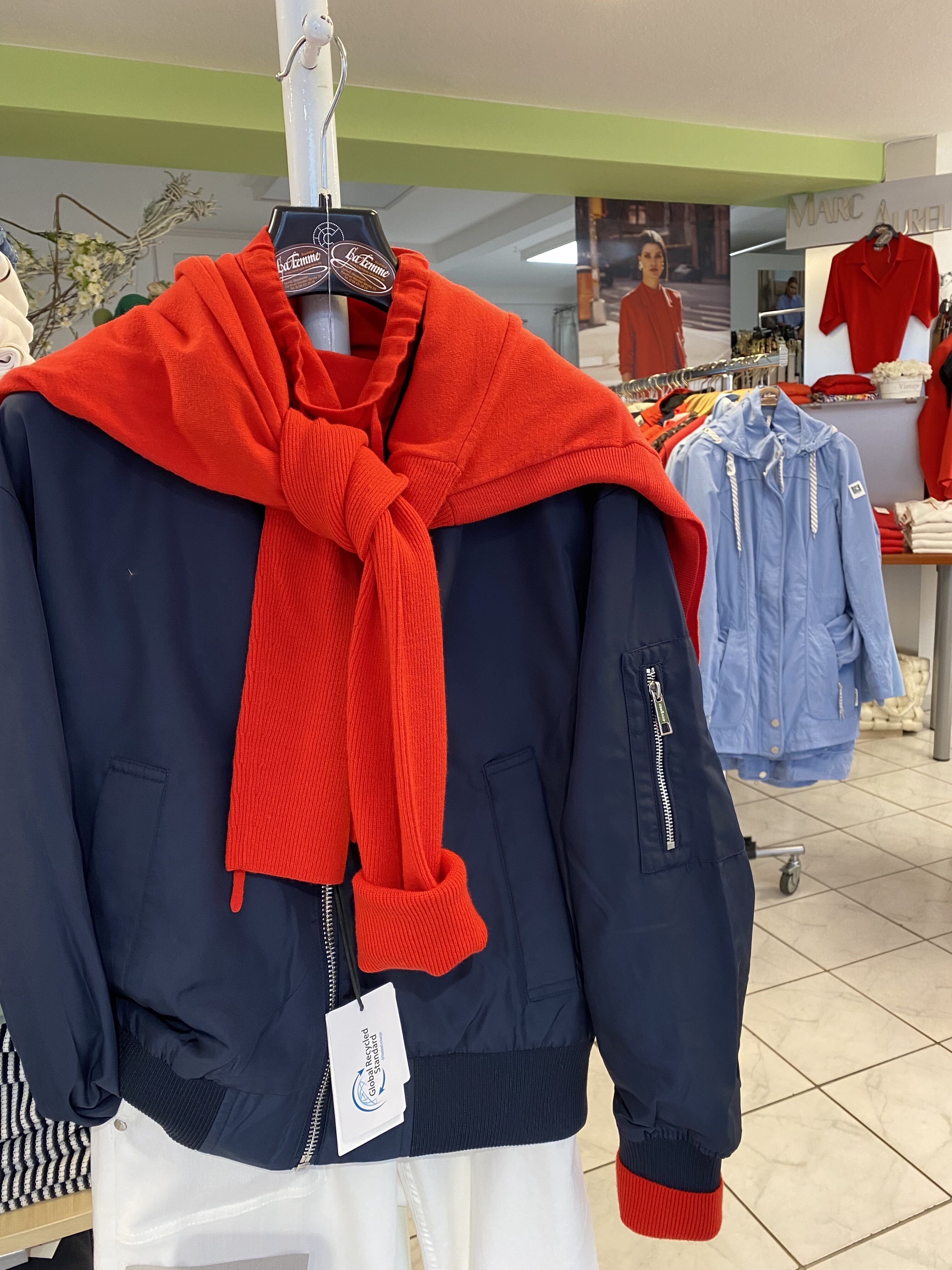 Eine blaue Jacke mit rotem Pullover darüber hängt in einem hellen Modegeschäft