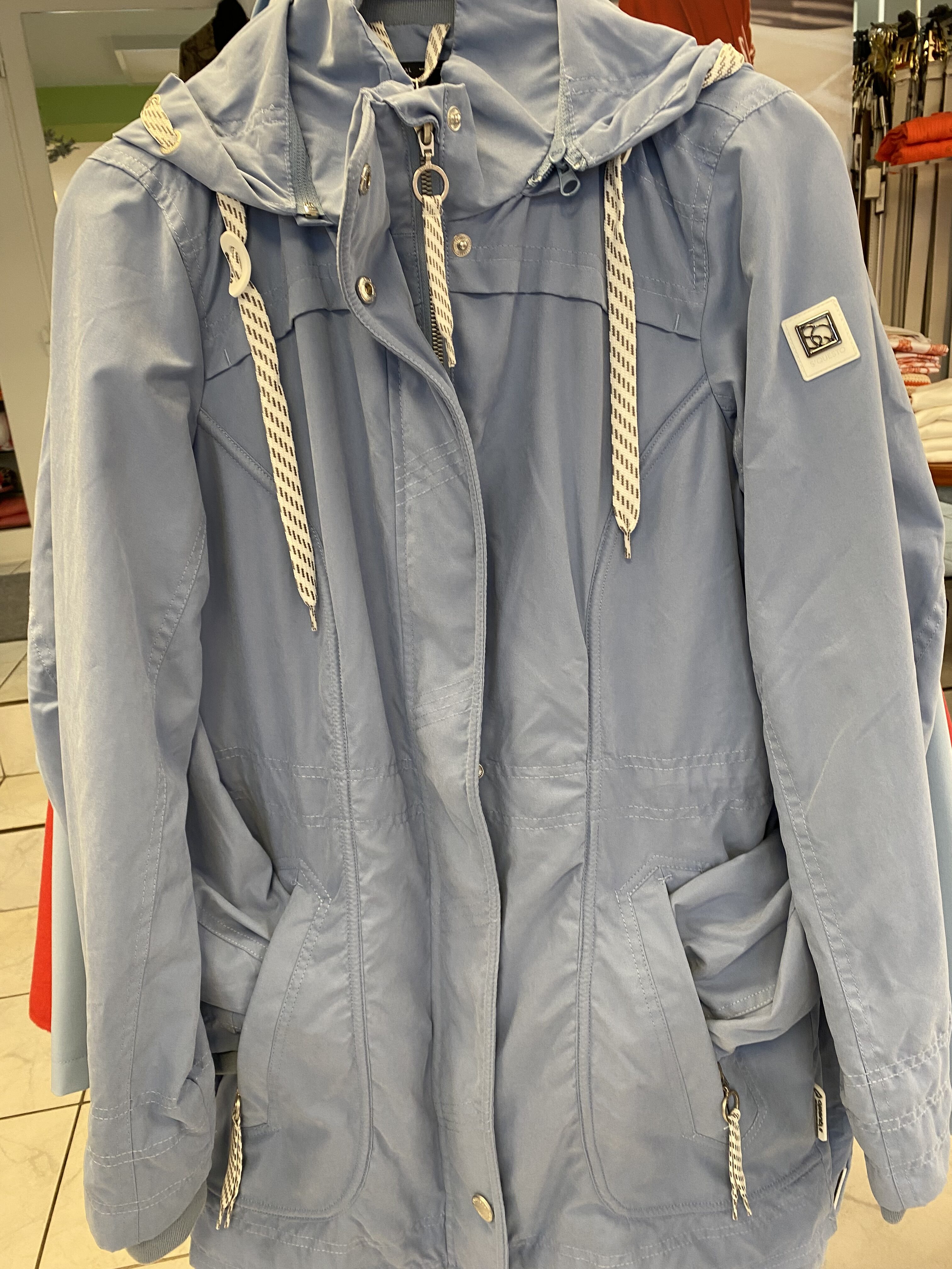 Eine hellblaue Jacke mit Kapuze, weißen Kordeln und silbernen Reißverschlüssen