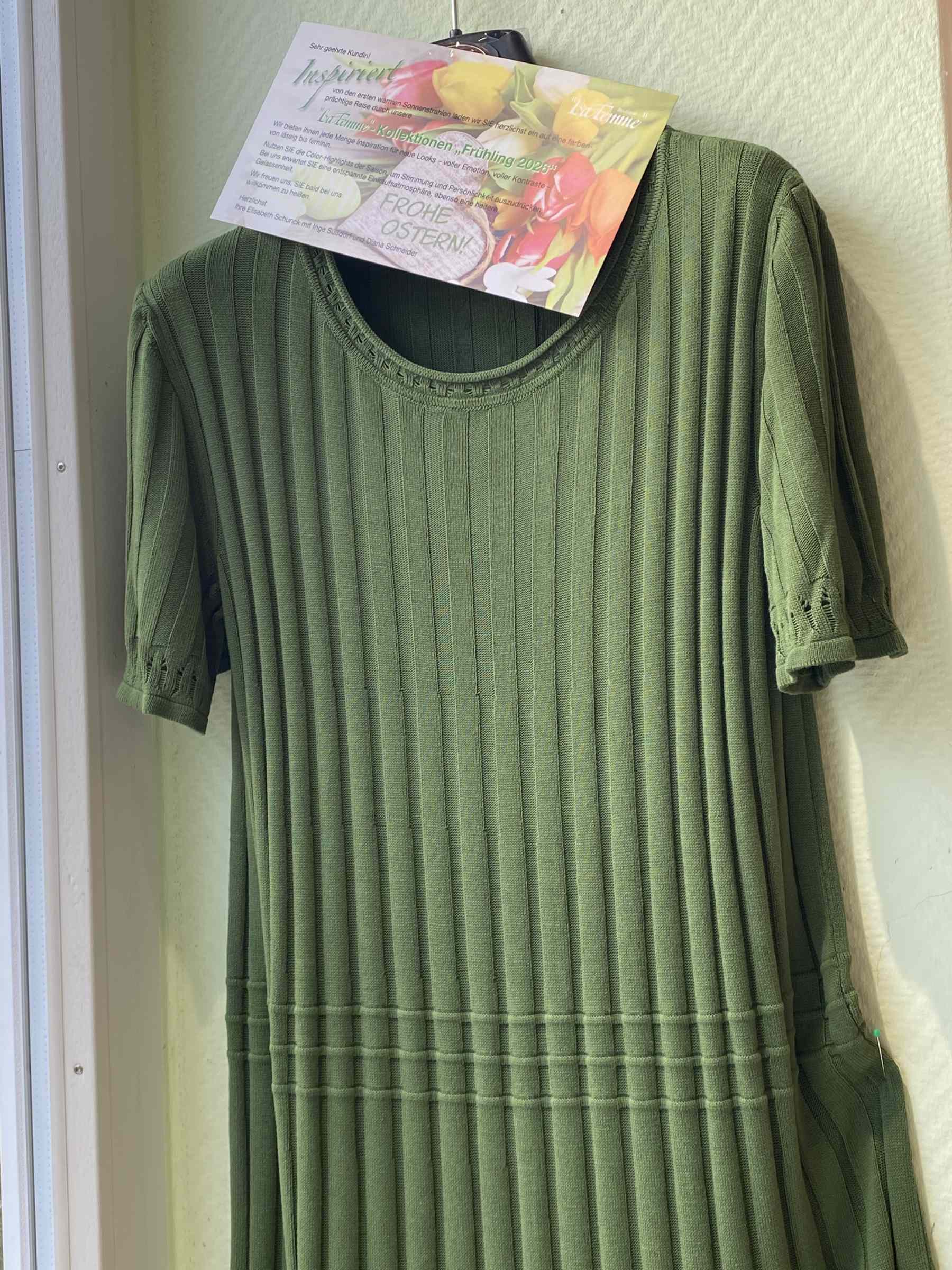 Grünes Kleid mit feinem Rippmuster auf Kleiderbügel und bunter Osterkarte drüber