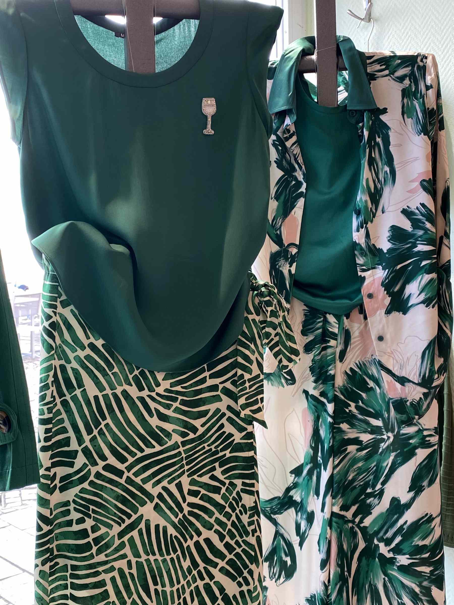 Zwei Schaufensterpuppen tragen grüne Outfits mit floralen und gemusterten Stoffen