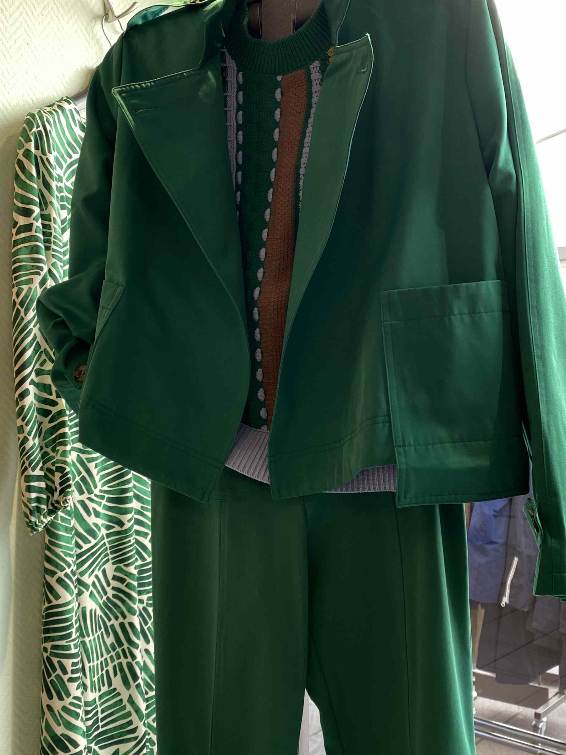 Ein grünes Damenkostüm mit gemustertem Pullover hängt vor einem gemusterten Kleid