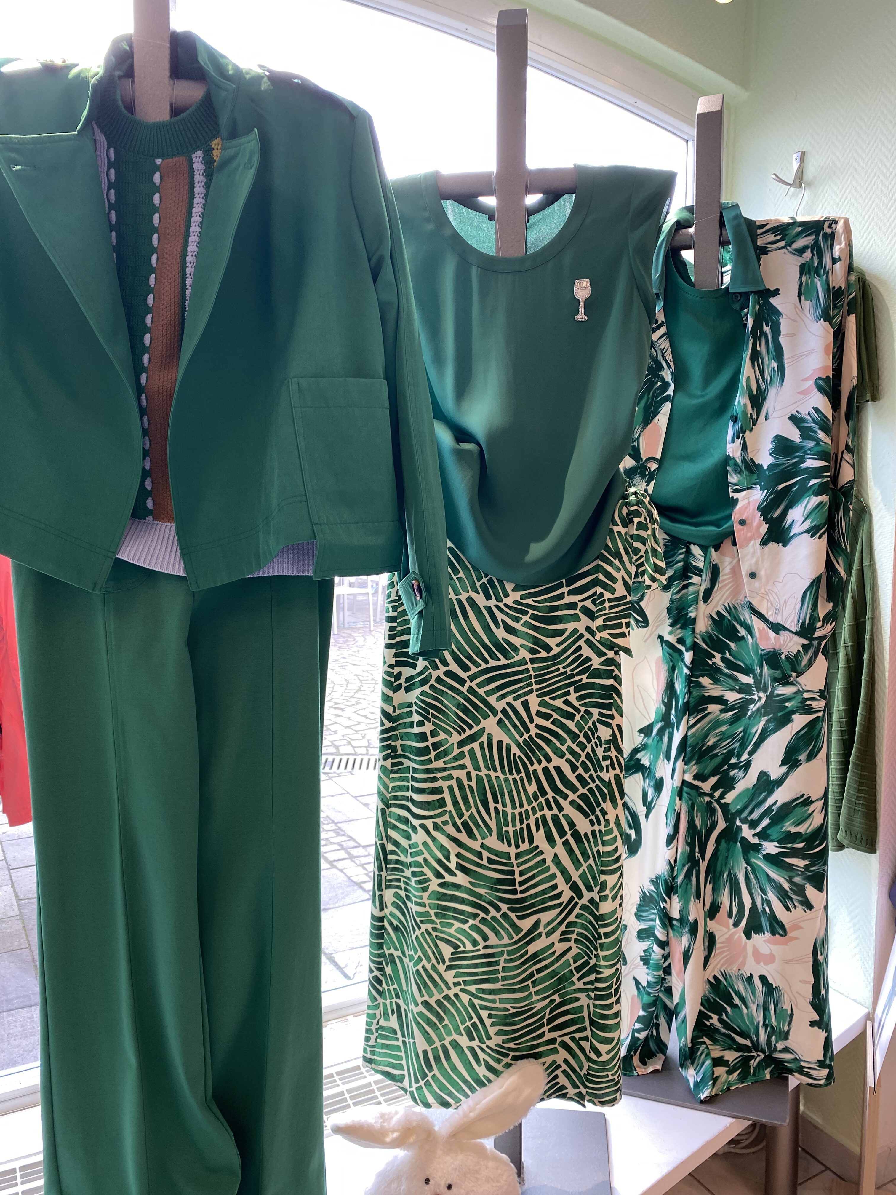 Drei Schaufensterpuppen tragen grüne Kleidung mit Mustern in einem hellen Schaufenster