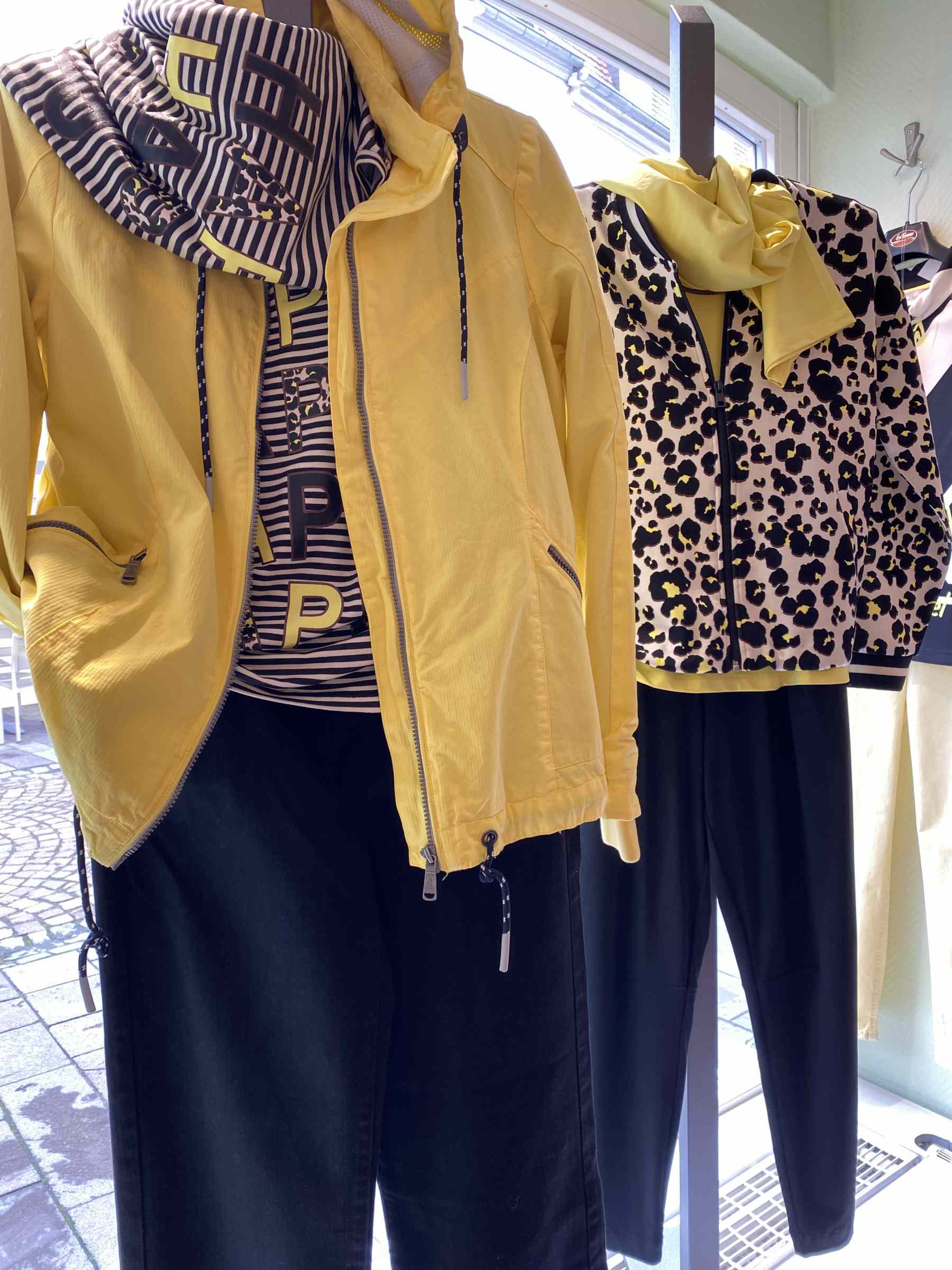 Zwei Schaufensterpuppen tragen gelbe Jacken mit schwarz gemusterten Oberteilen und schwarzen Hosen