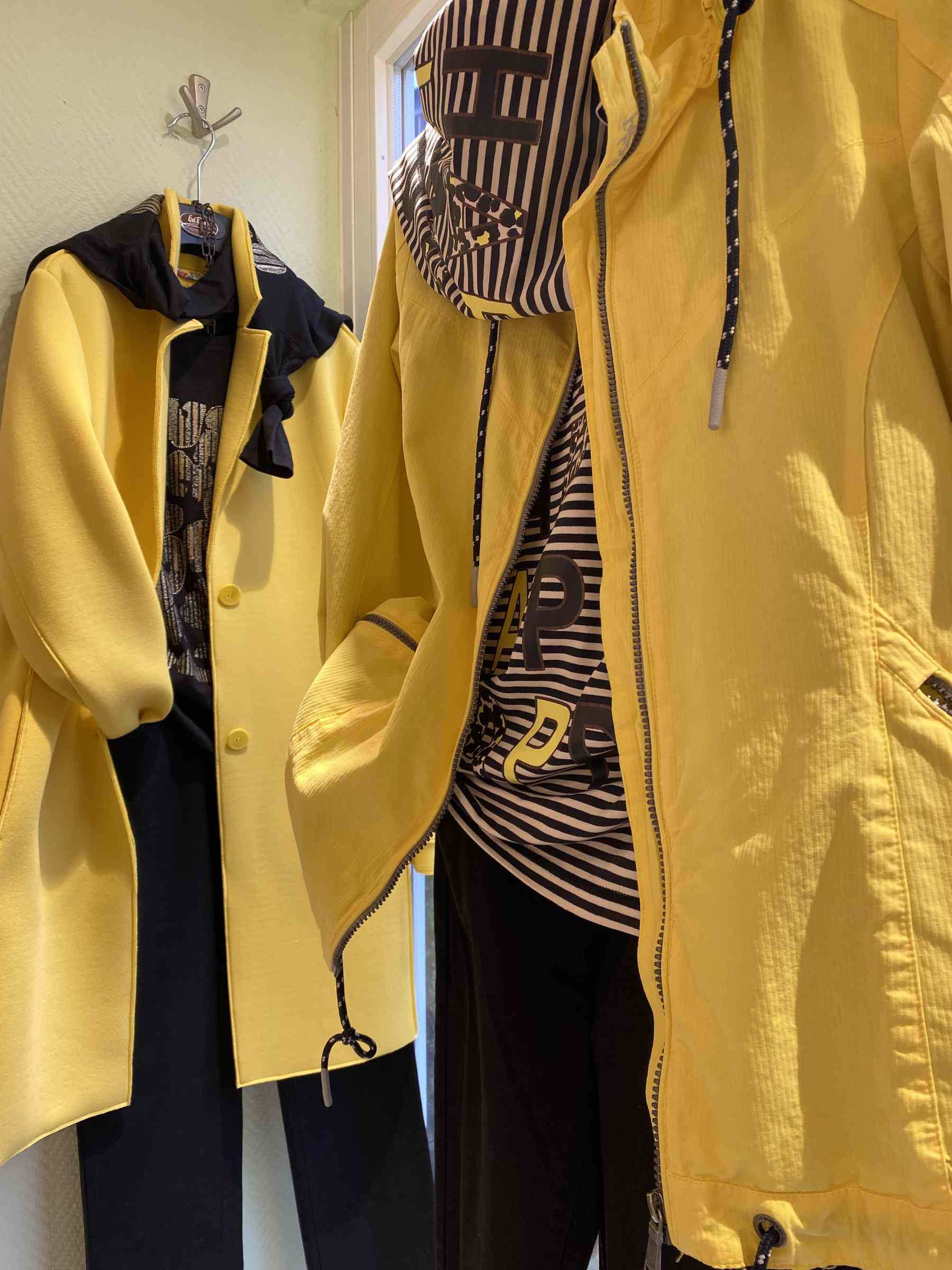 Zwei gelbe Jacken mit schwarzen und gestreiften Oberteilen hängen an der Wand