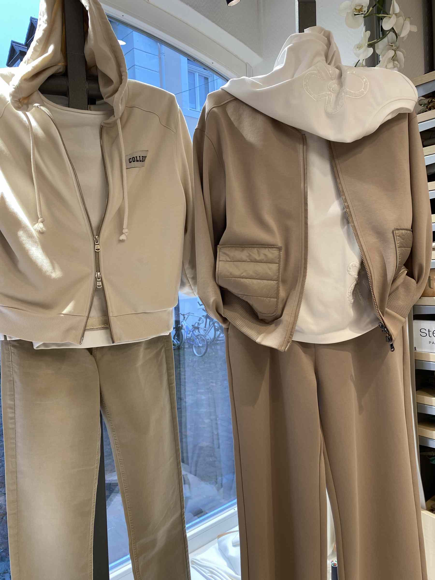 Zwei Schaufensterpuppen tragen beige und weiße Freizeitkleidung mit Kapuzenpullis