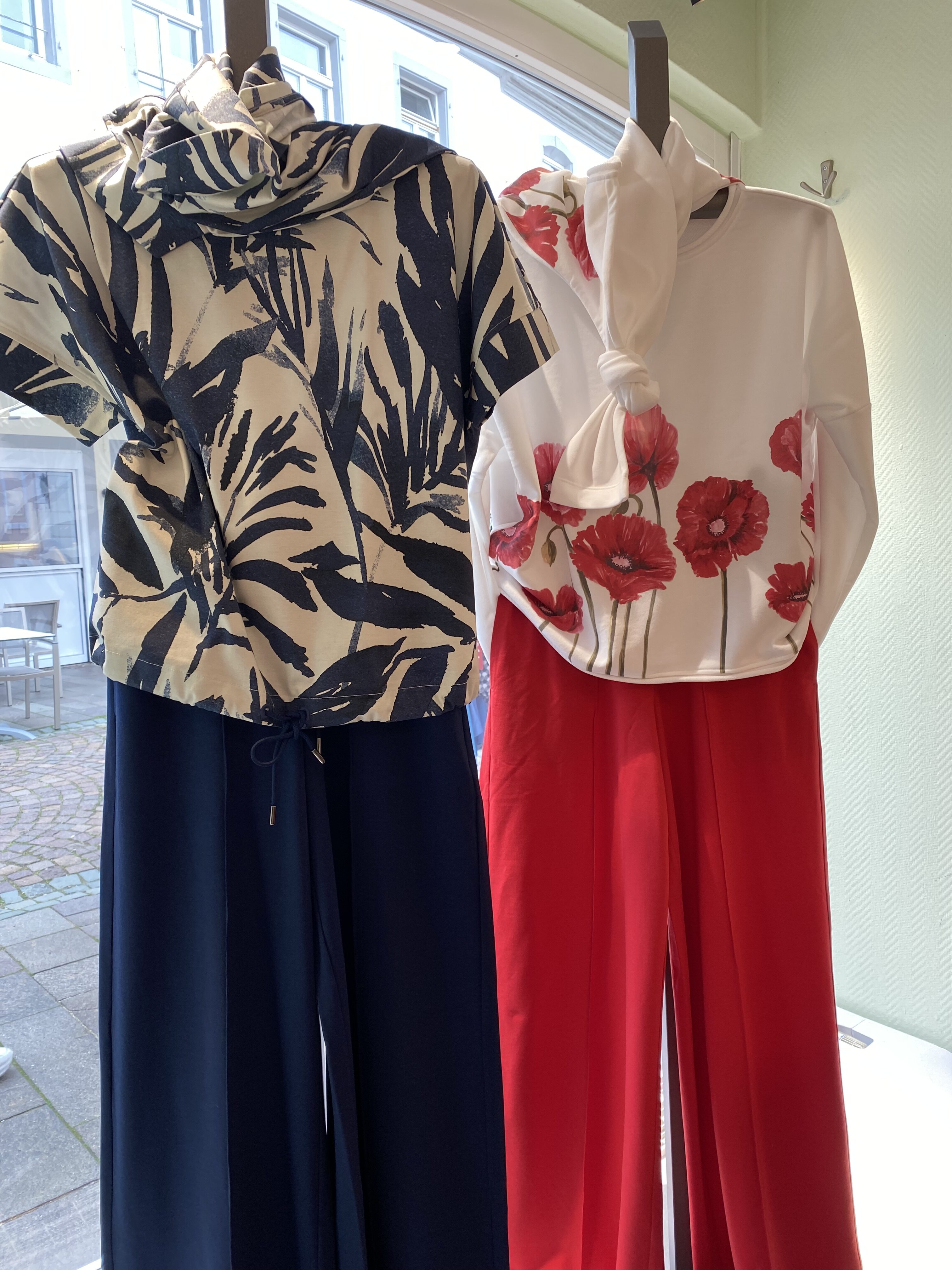 Zwei Schaufensterpuppen tragen farbenfrohe Outfits mit floralen Mustern und weitem Schnitt