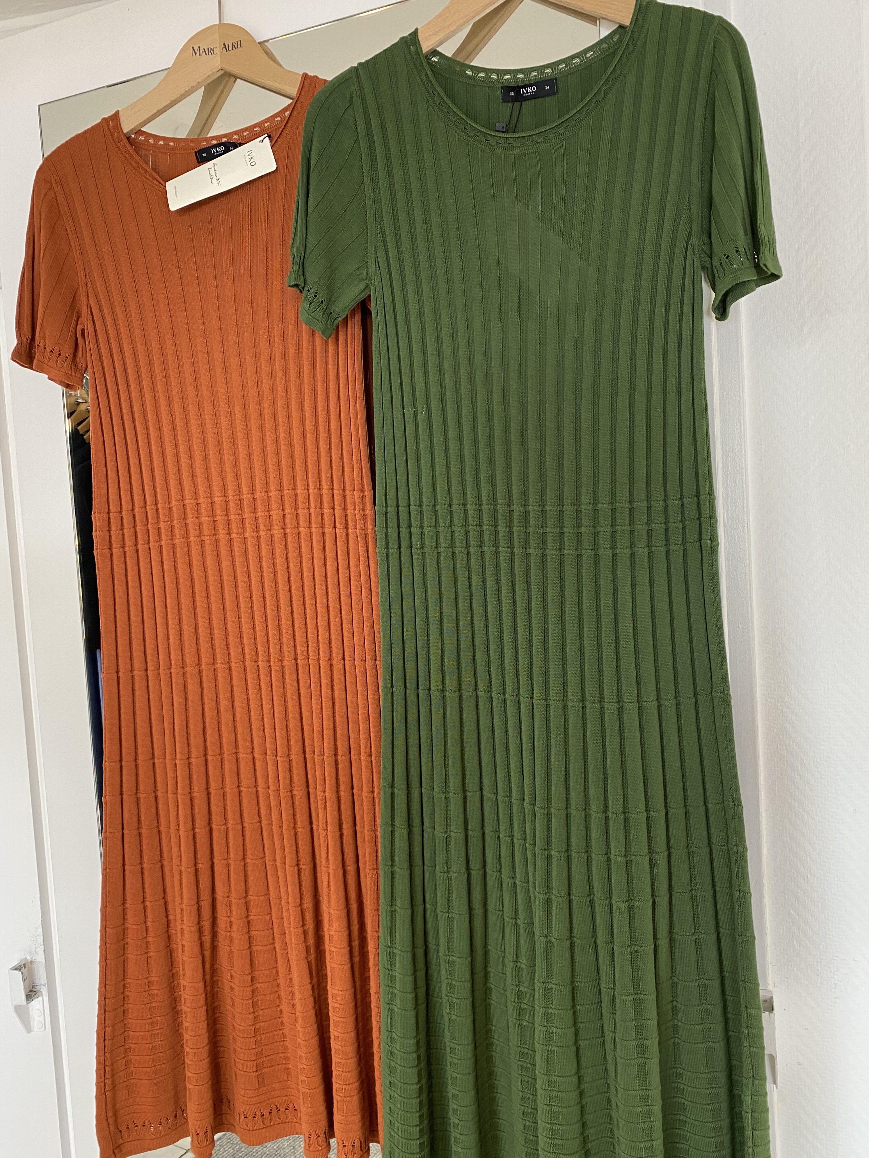 Ein orangefarbenes und ein grünes Kleid mit geripptem Muster hängen nebeneinander