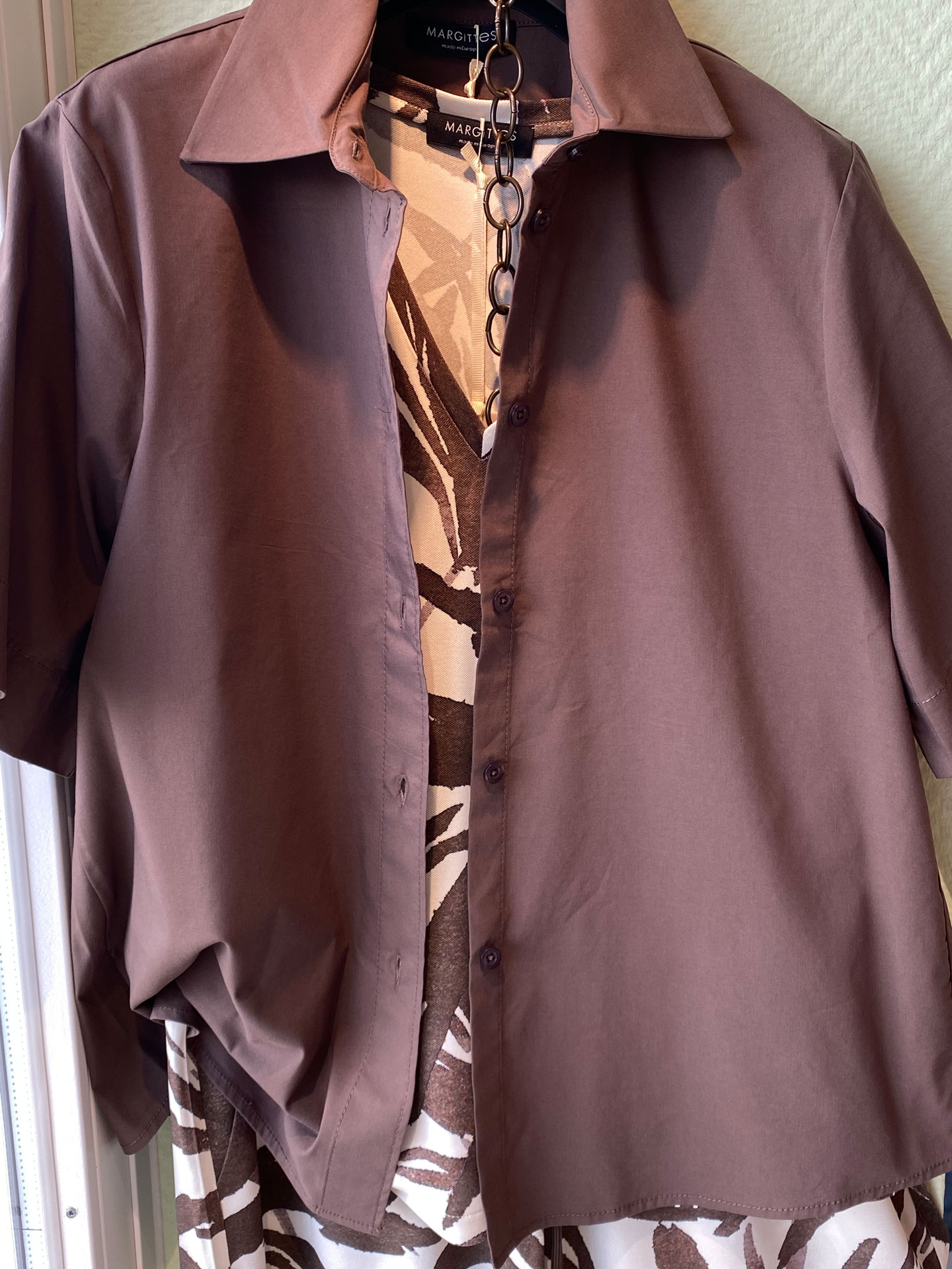 Braune Bluse über gemustertem Kleid in Beige und Braun am Bügel hängend