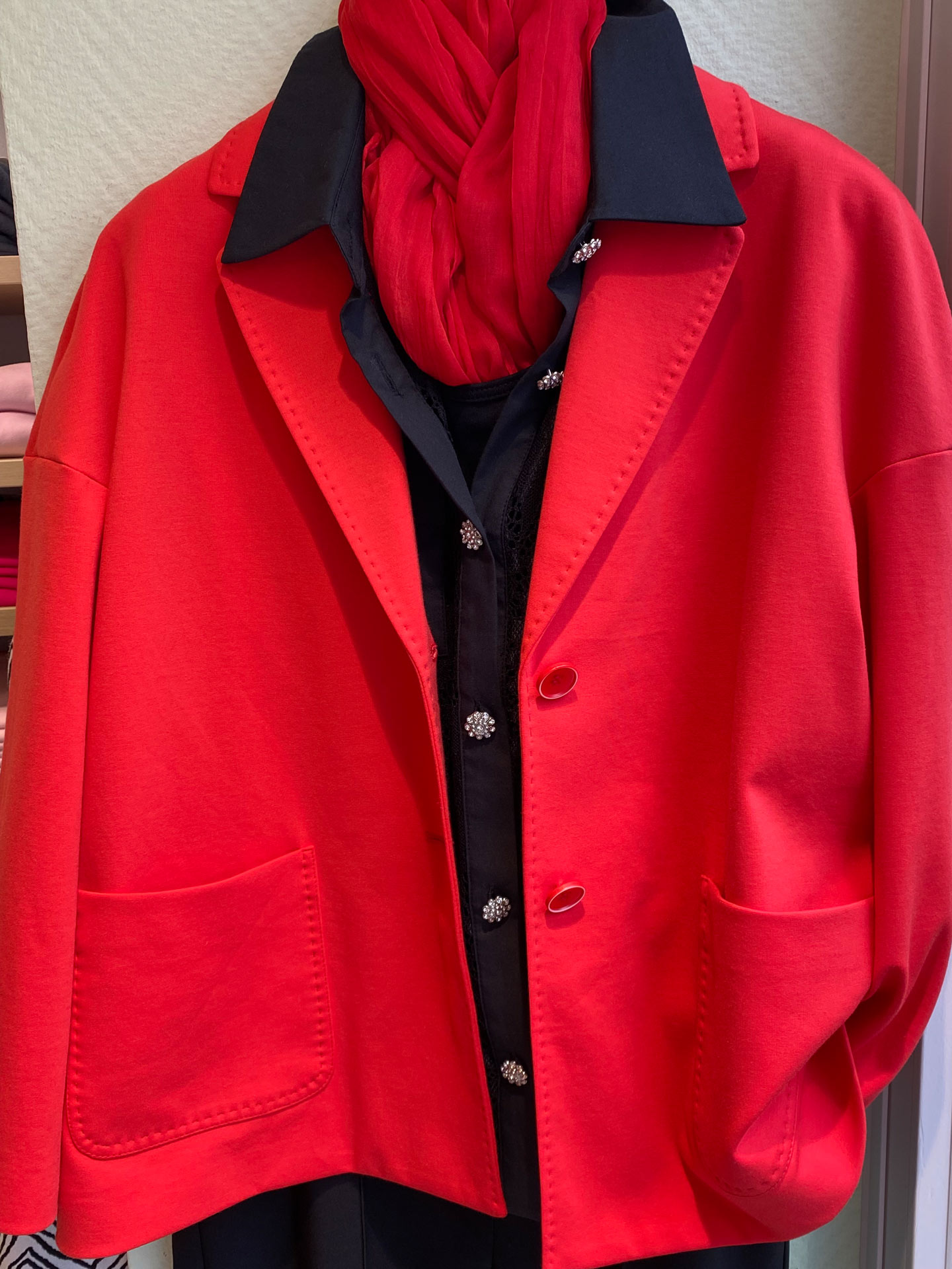 Rote Jacke mit rotem Schal und schwarzer Bluse mit Schmuckknöpfen am Bügel