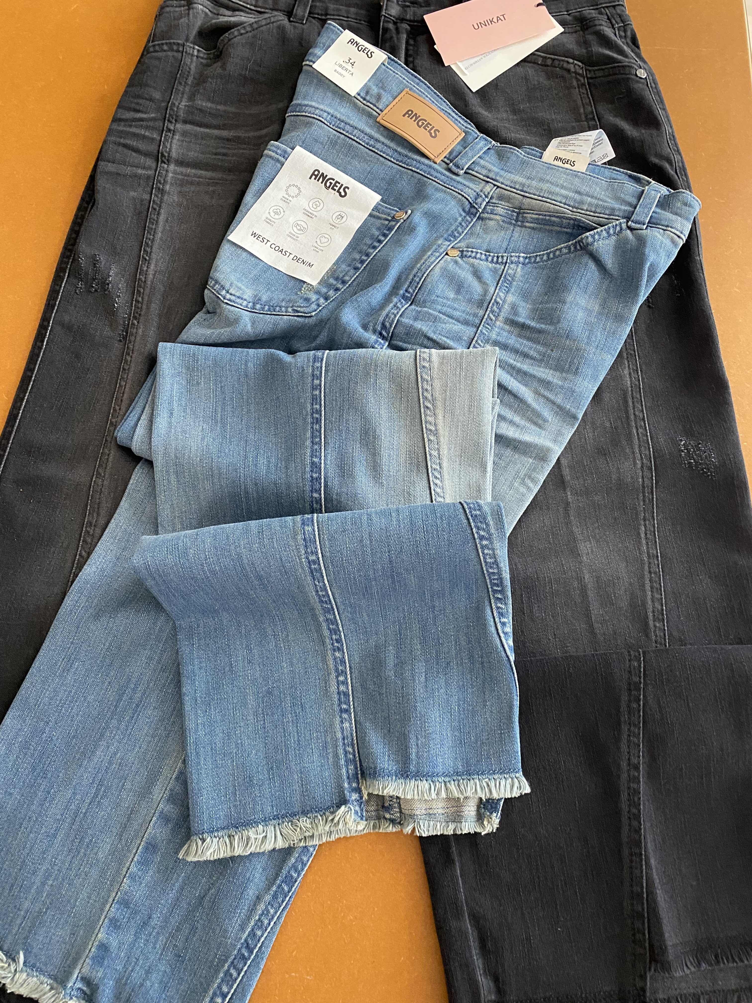 Blaue und schwarze Angels Jeans mit Etiketten liegen auf orangefarbenem Untergrund
