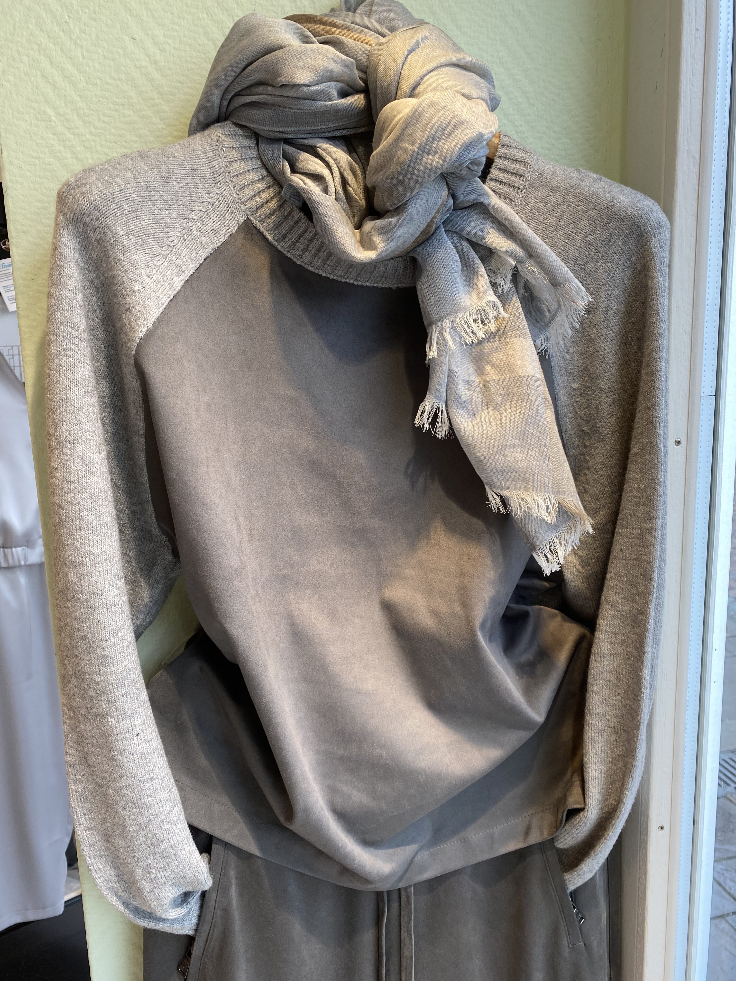 Graue Schaufensterpuppe mit Strickpullover und drapiertem Schal mit Fransen