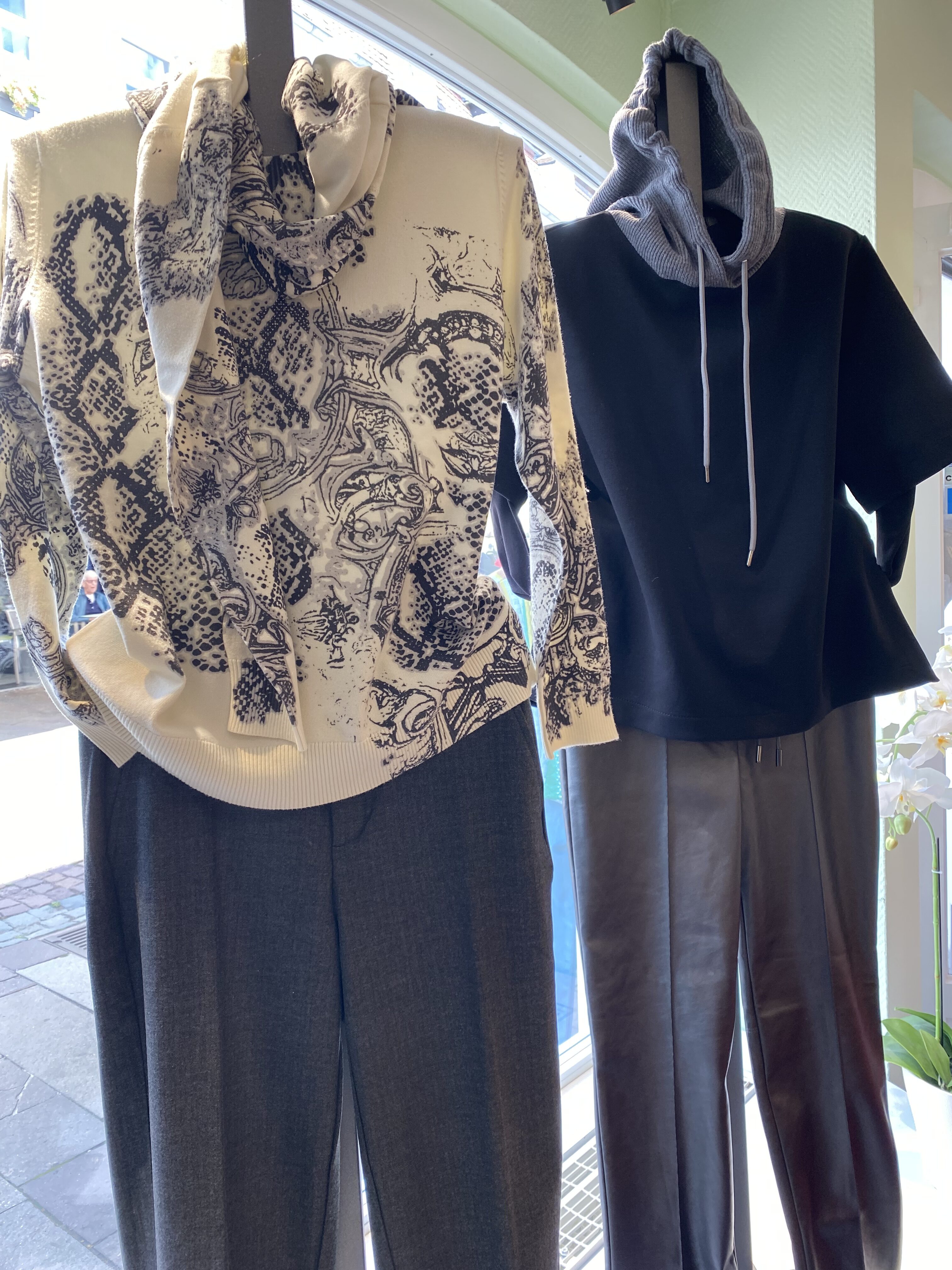 Zwei Schaufensterpuppen mit gemustertem Pullover und schwarzem Kapuzenshirt