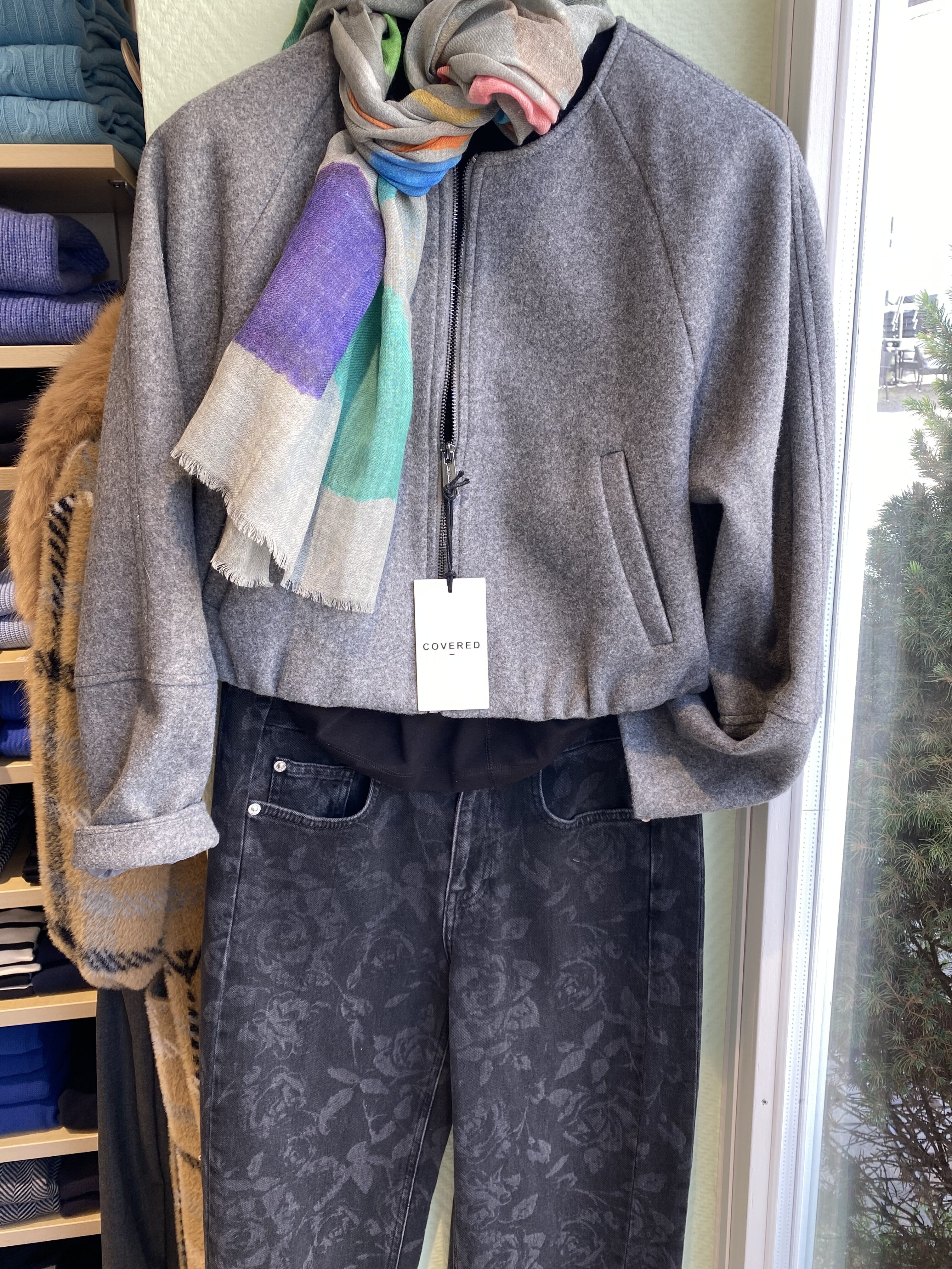 Graue Wolljacke mit buntem Schal und dunkler Jeans mit Blumenmuster im Laden